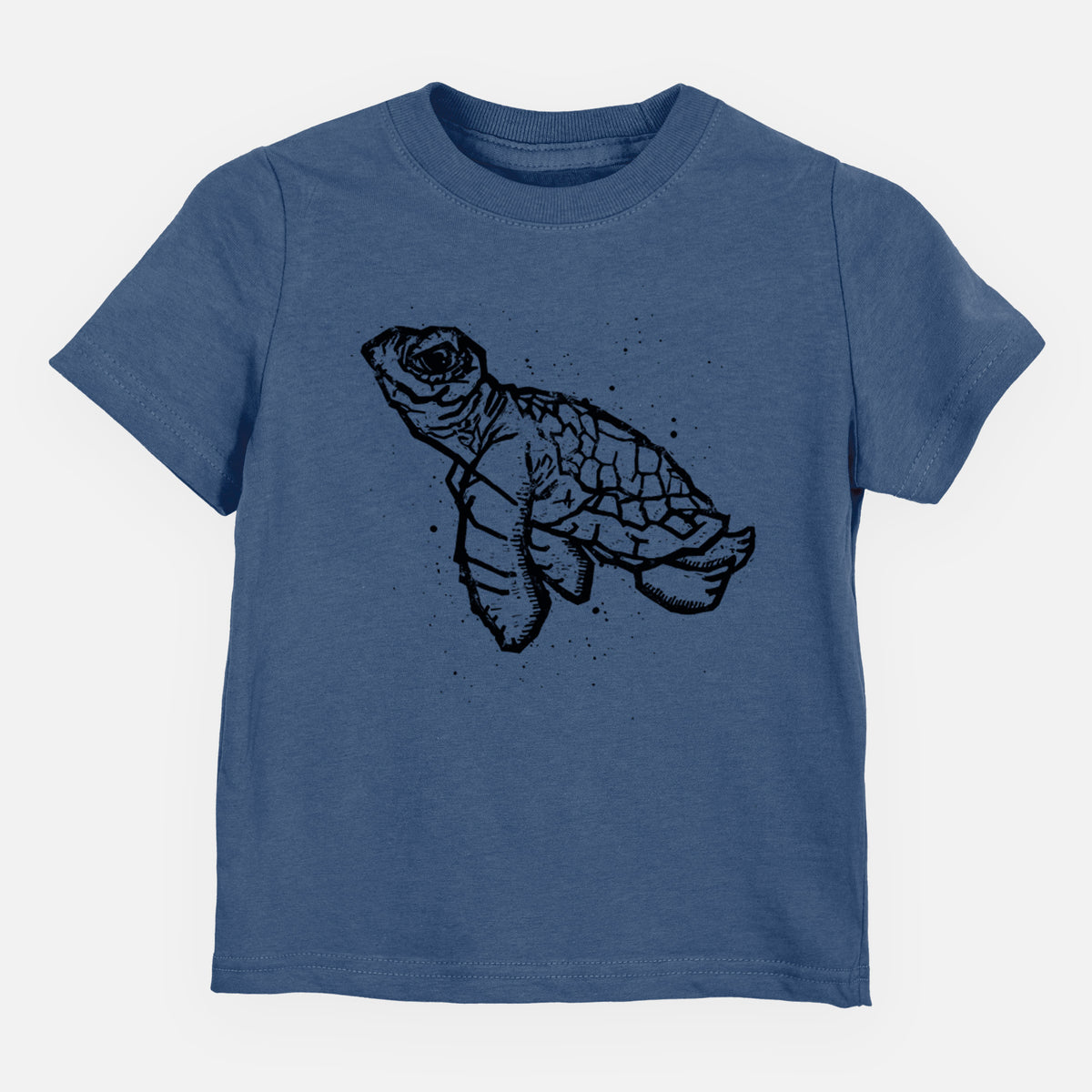 Indigo blue toddler t-shirt laid flat, printed with a black linocut-style illustration of a baby sea turtle with a patterned shell and ink splatters.