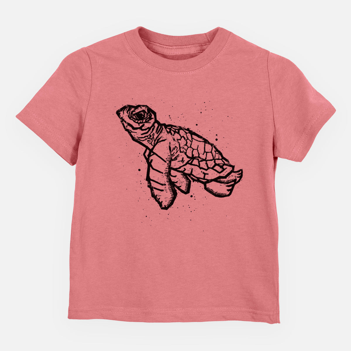 Mauve pink toddler t-shirt laid flat, printed with a black linocut-style illustration of a baby sea turtle with a patterned shell and ink splatters.