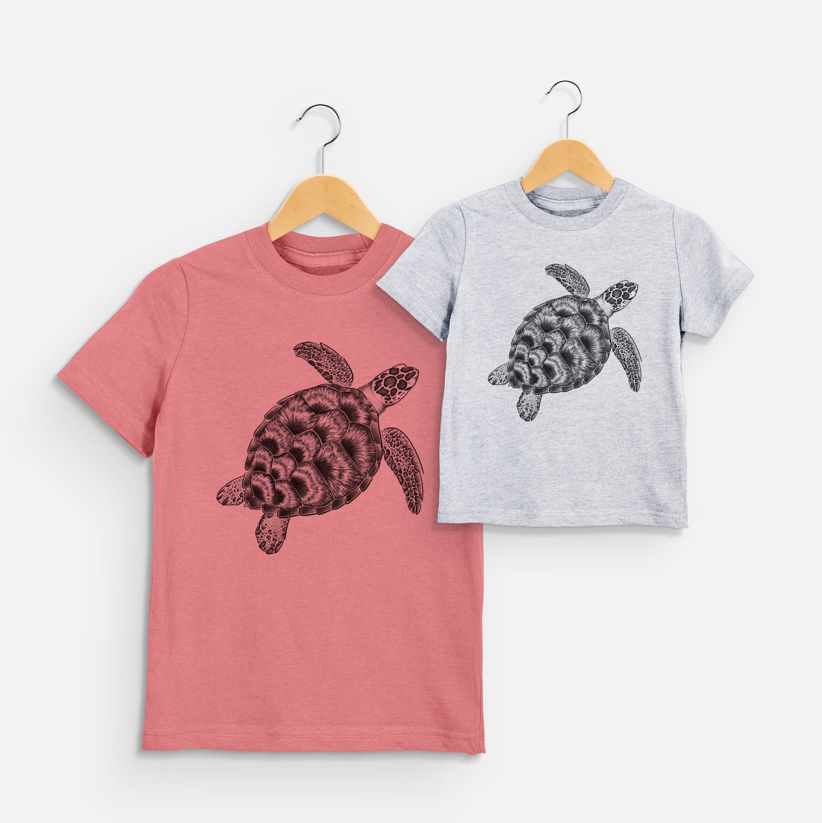Two youth t-shirts in different colors on hangers, printed with a detailed black ink illustration of a loggerhead sea turtle swimming, seen from above.