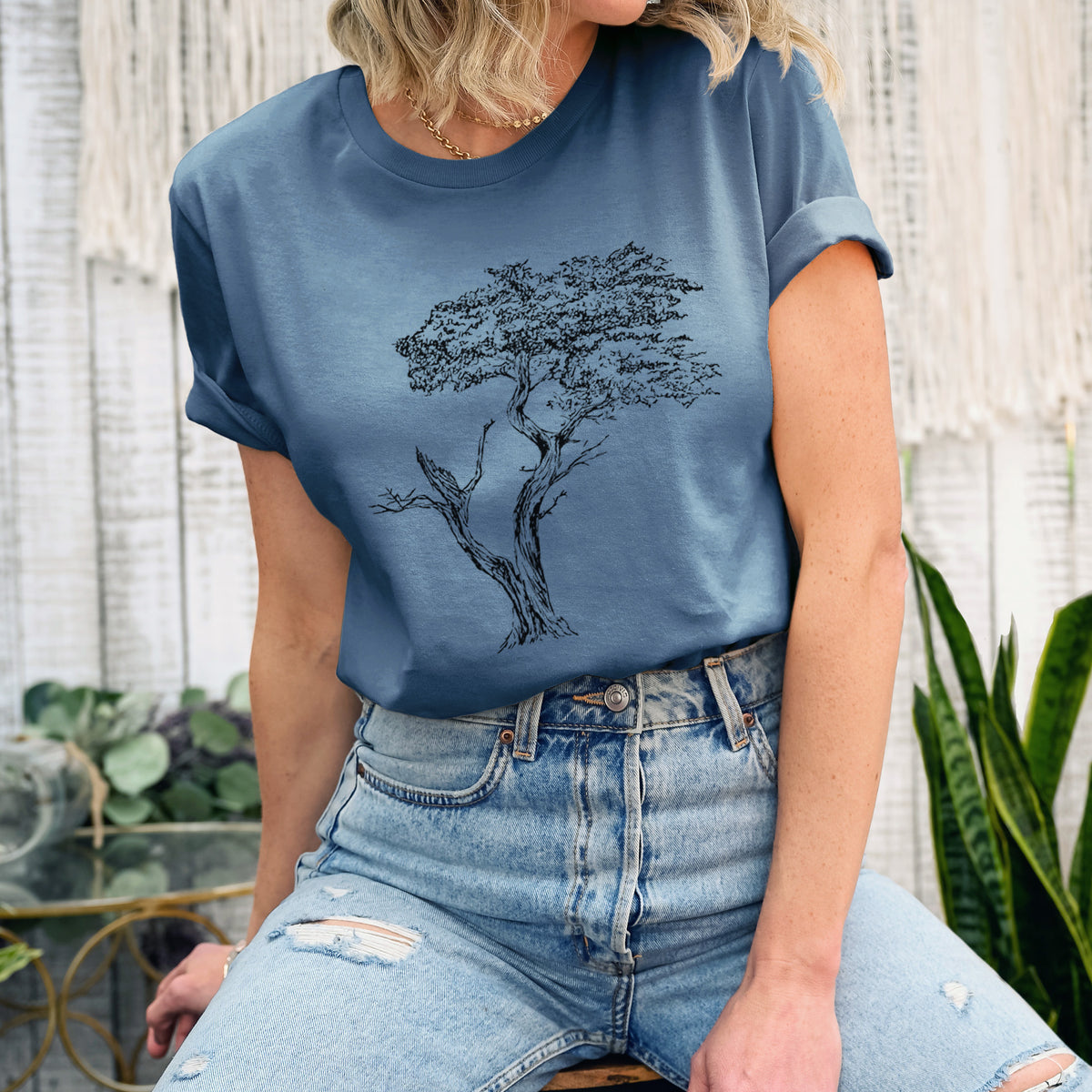 Woman wearing a steel blue lightweight cotton t-shirt printed with a black ink illustration of the windswept Lone Cypress tree on a rocky outcrop.
