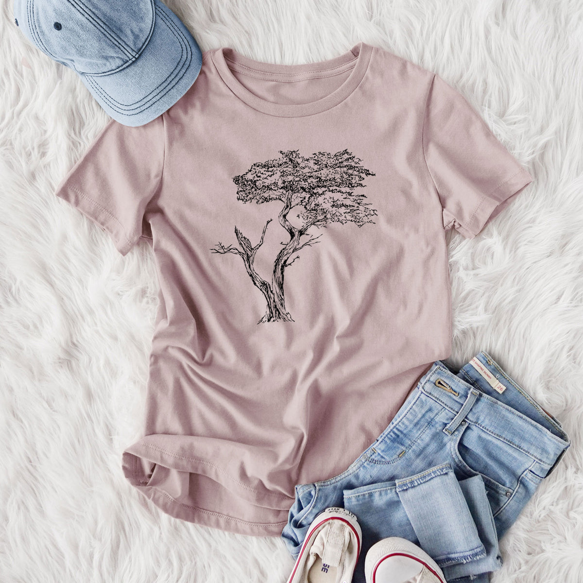 Women's relaxed fit cotton t-shirt printed with a black ink illustration of the windswept Lone Cypress tree on a rocky outcrop, styled flat on a white faux fur rug with jeans.