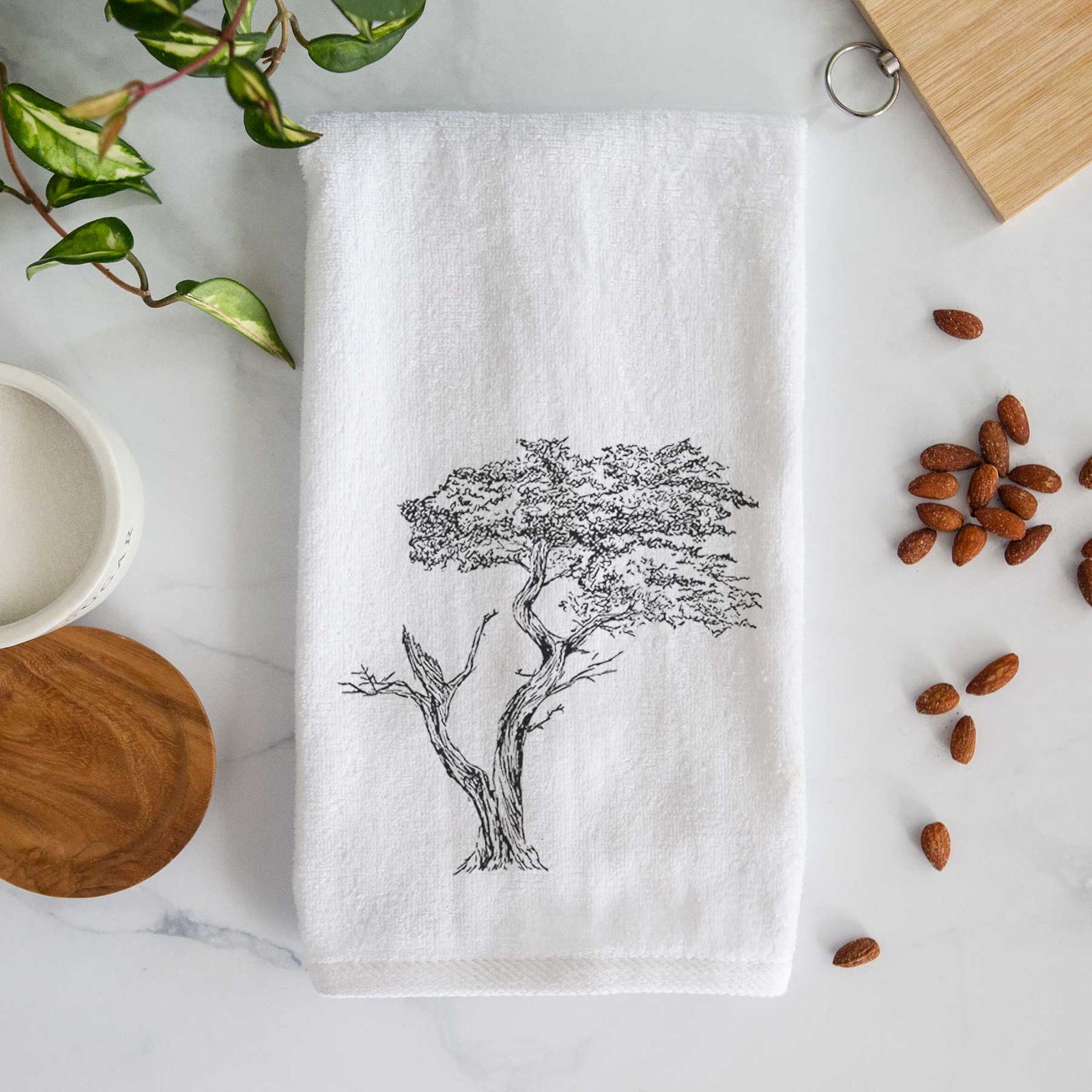 White hand towel printed with a black ink illustration of the windswept Lone Cypress tree on a rocky outcrop.