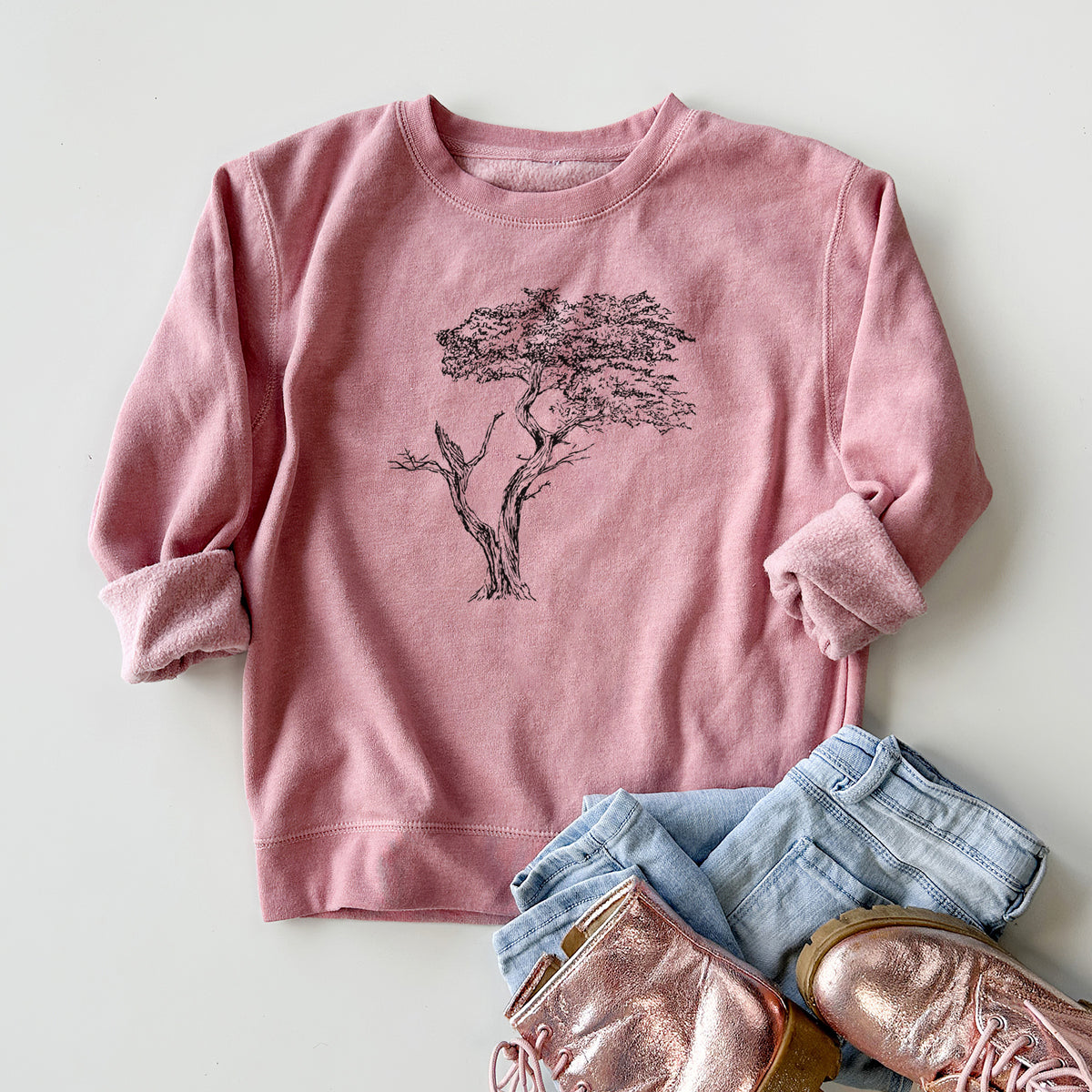 Youth crewneck sweatshirt printed with a black ink illustration of the windswept Lone Cypress tree on a rocky outcrop, styled flat with jeans and boots.
