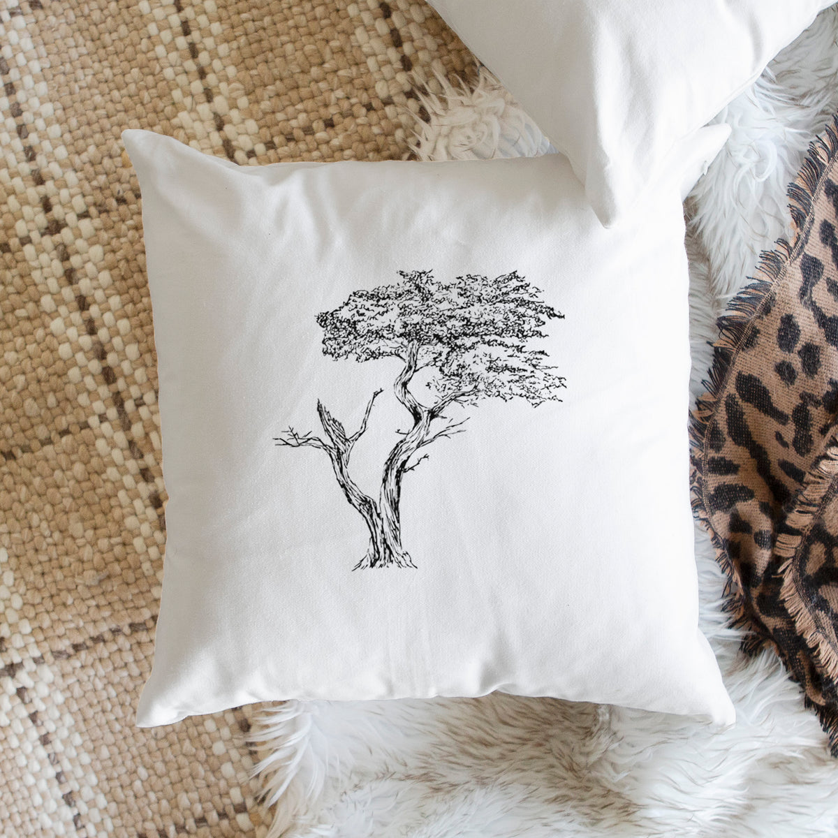 White pillow cover printed with a black ink illustration of the windswept Lone Cypress tree on a rocky outcrop, on a woven chair.