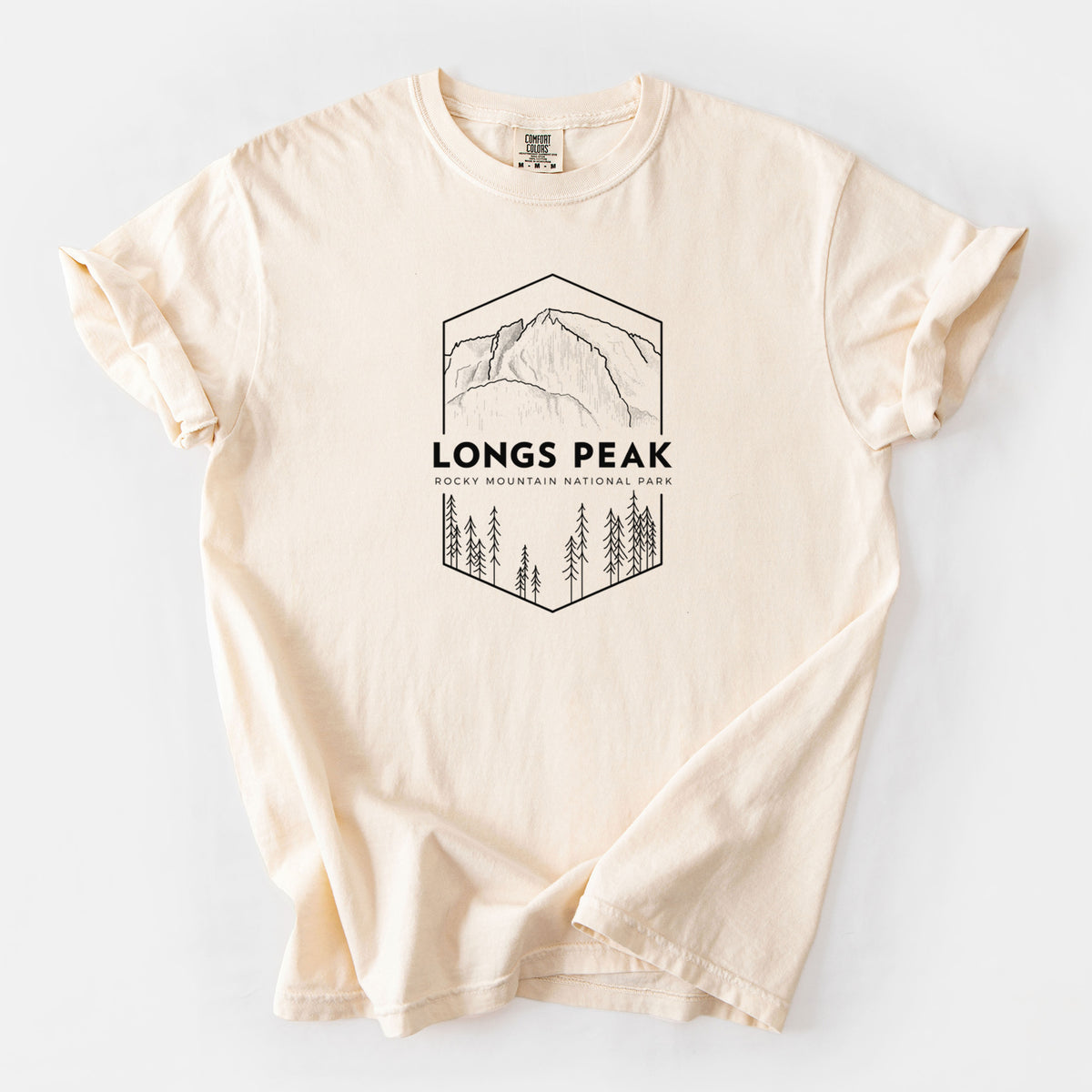 Ivory Comfort Colors t-shirt laid flat, printed with a black line art badge of Longs Peak above a pine forest, with the words Longs Peak, Rocky Mountain National Park.
