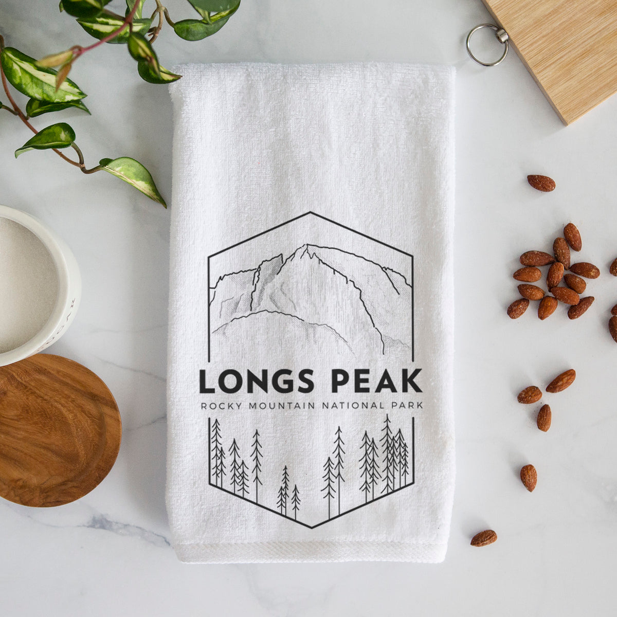 White hand towel printed with a black line art badge of Longs Peak above a pine forest, with the words Longs Peak, Rocky Mountain National Park.