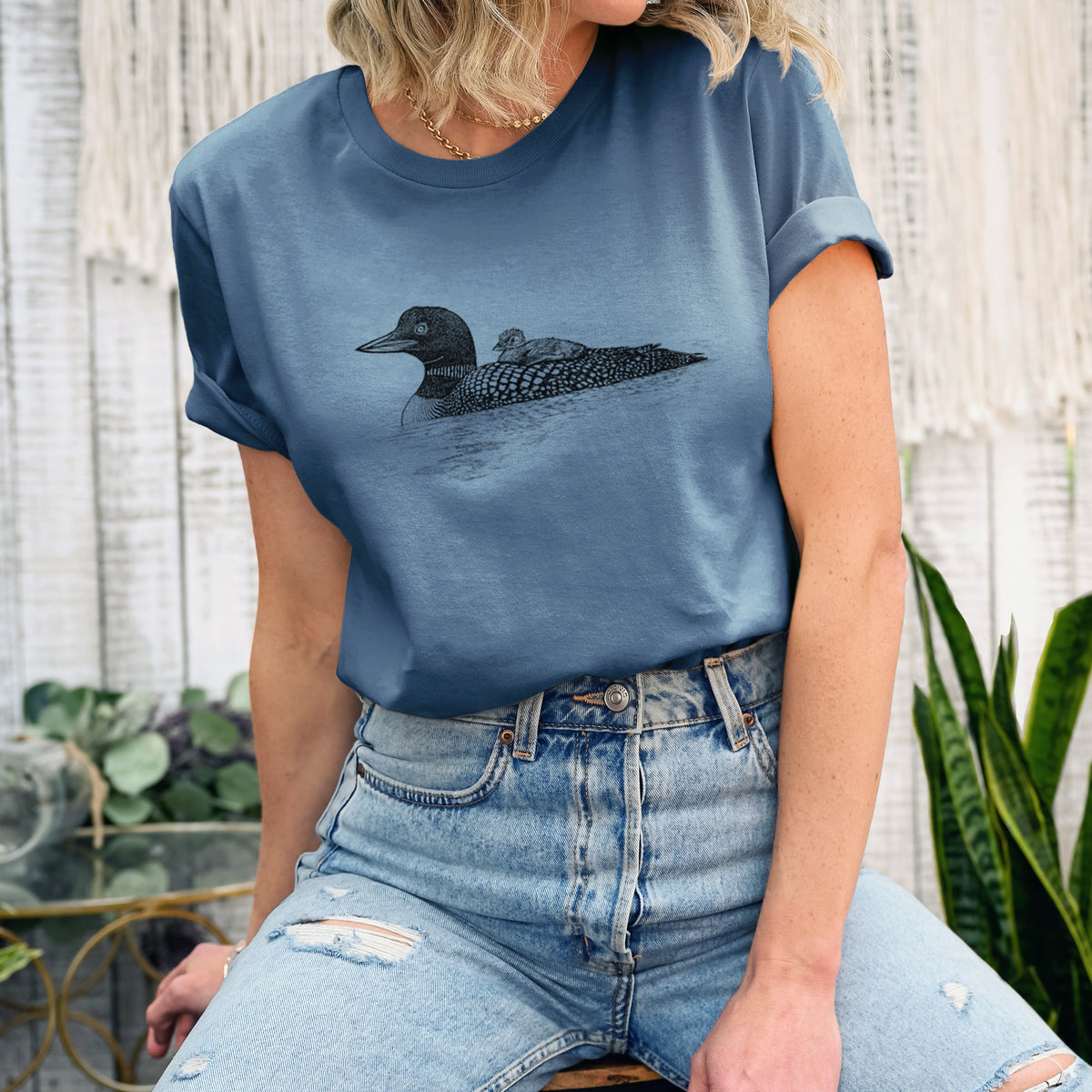 Woman wearing a steel blue lightweight cotton t-shirt printed with a black ink sketch of a common loon floating on water with a chick riding on its back.