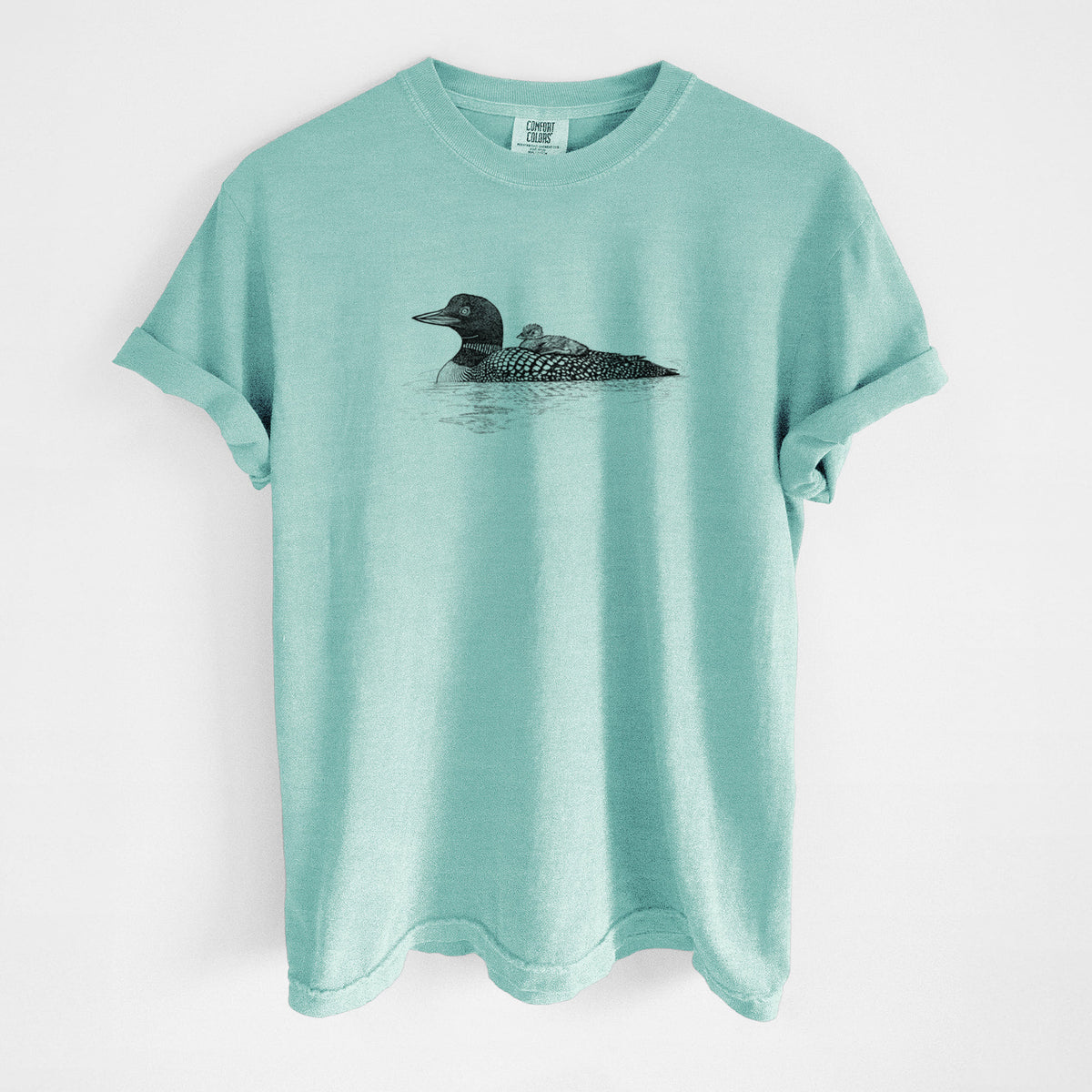 Chalky mint Comfort Colors t-shirt laid flat, printed with a black ink sketch of a common loon floating on water with a chick riding on its back.
