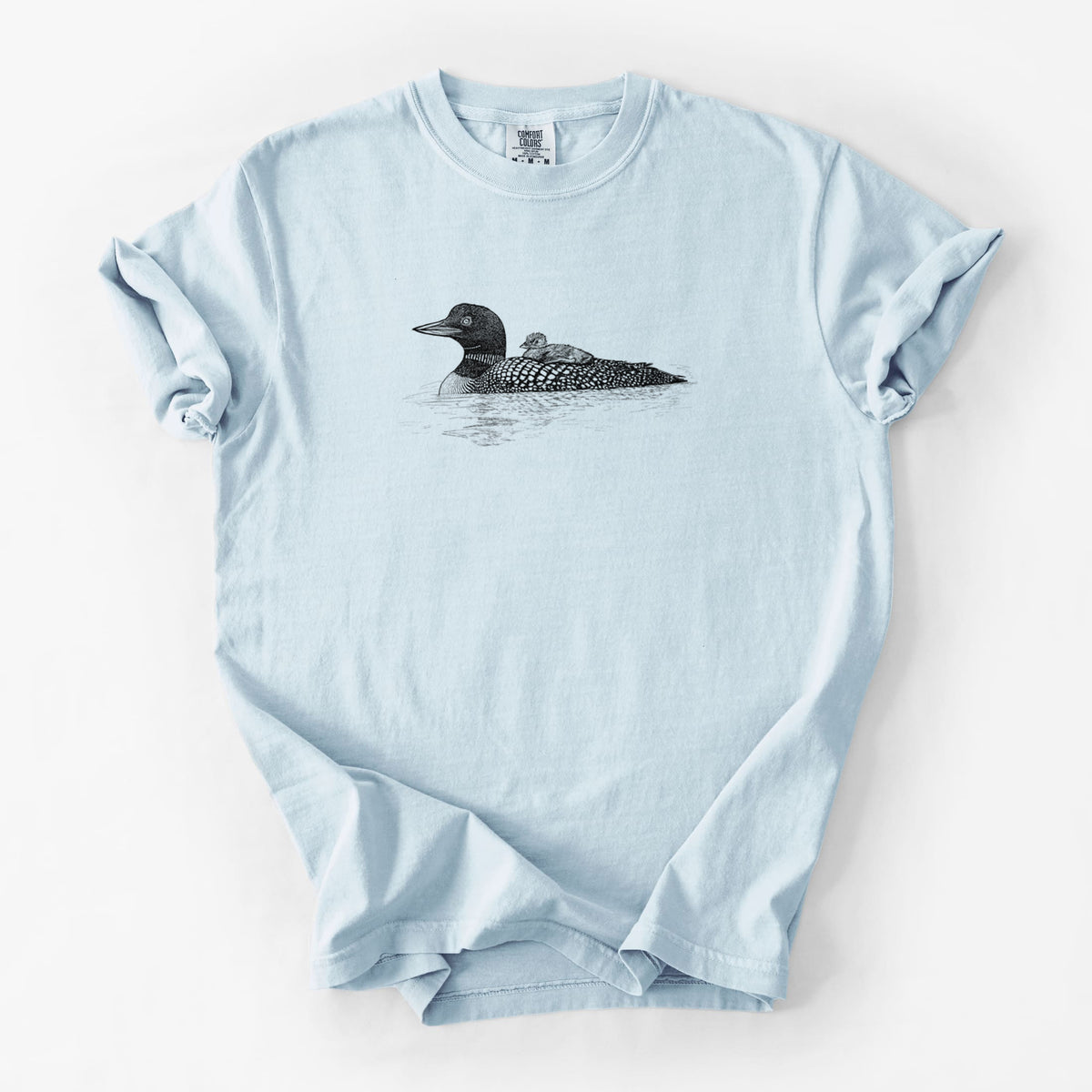 Chambray blue Comfort Colors t-shirt laid flat, printed with a black ink sketch of a common loon floating on water with a chick riding on its back.