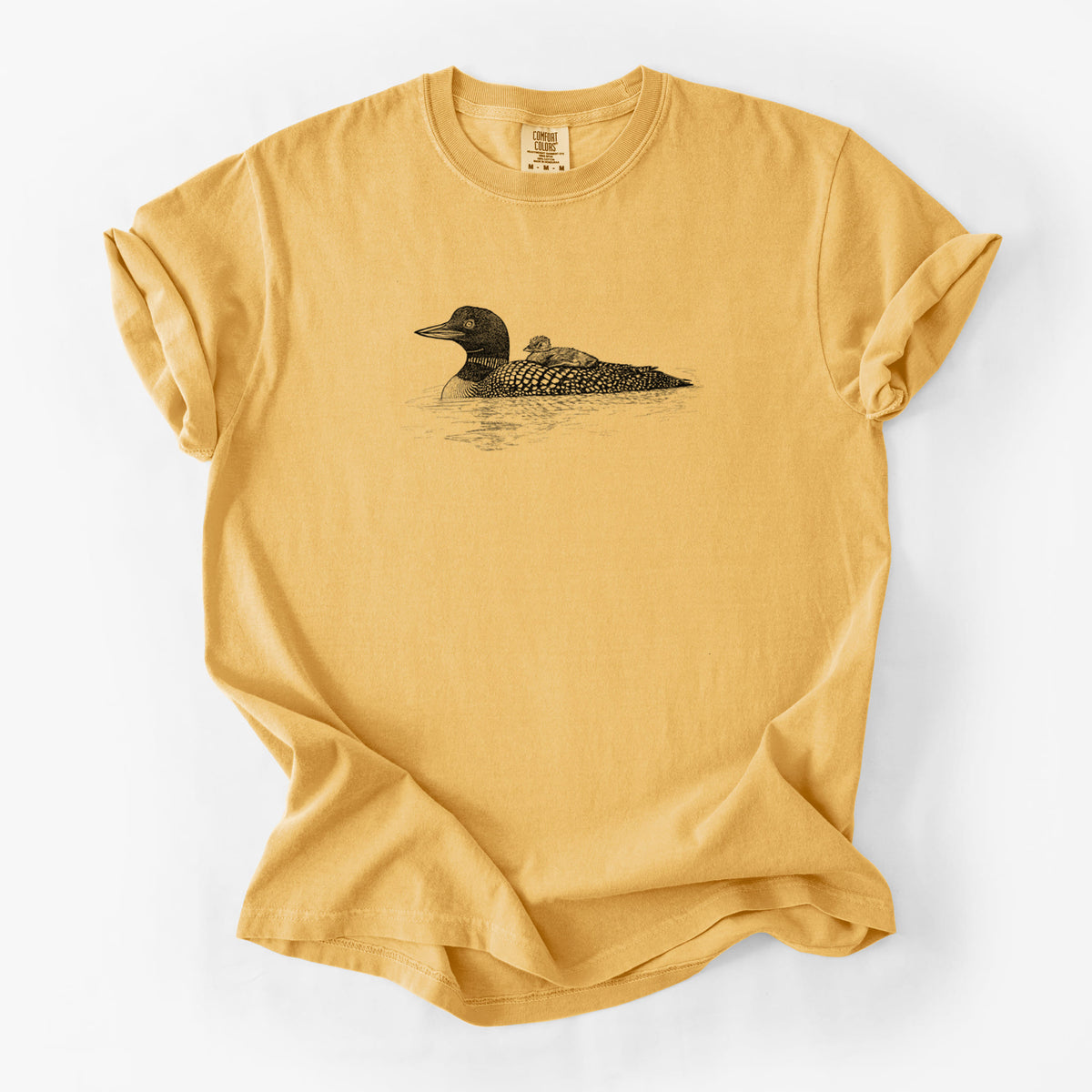 Golden wheat yellow Comfort Colors t-shirt laid flat, printed with a black ink sketch of a common loon floating on water with a chick riding on its back.