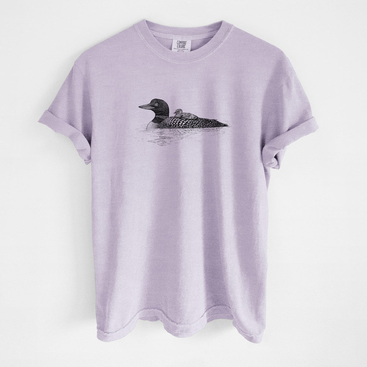 Orchid purple Comfort Colors t-shirt laid flat, printed with a black ink sketch of a common loon floating on water with a chick riding on its back.