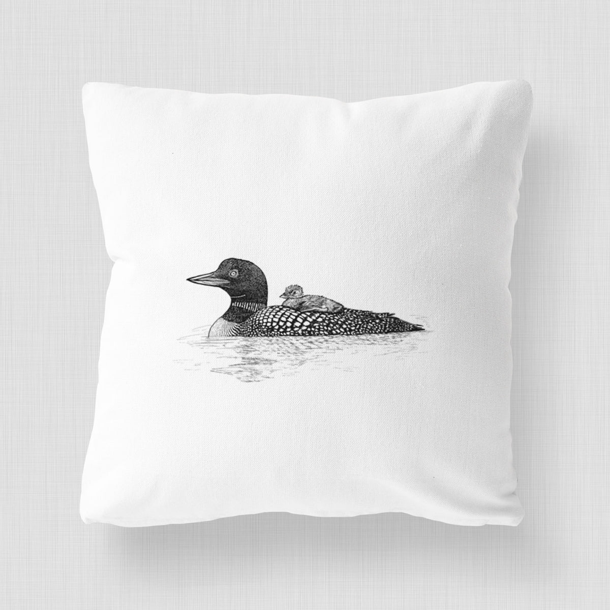 White pillow cover printed with a black ink sketch of a common loon floating on water with a chick riding on its back.