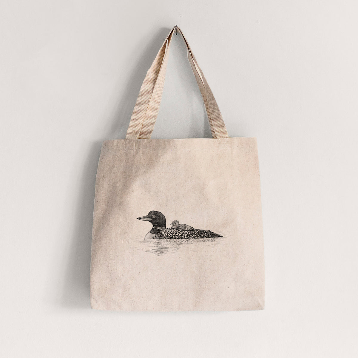 Natural canvas tote bag printed with a black ink sketch of a common loon floating on water with a chick riding on its back.