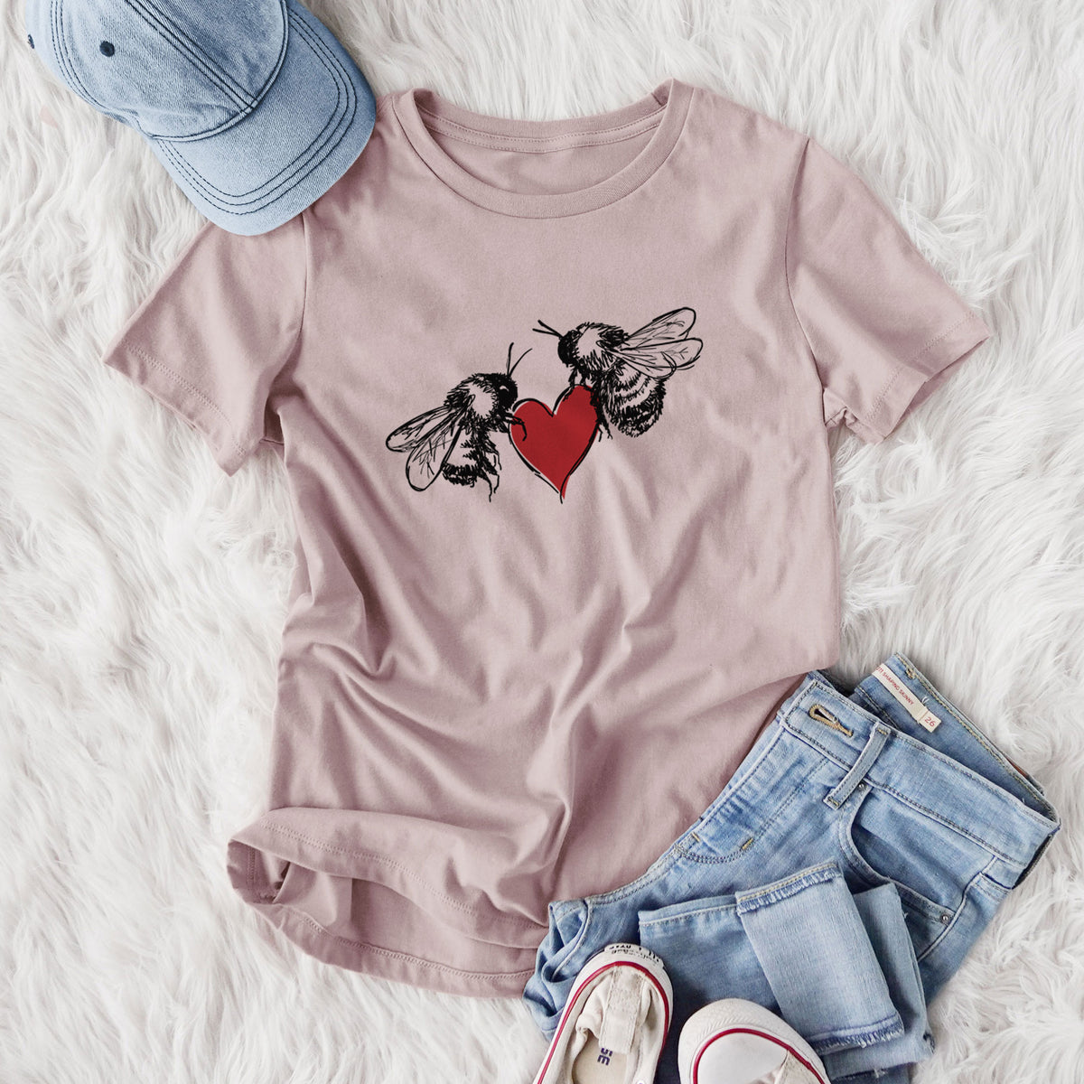 Women's relaxed fit cotton t-shirt printed with a black ink illustration of two bees facing each other with a red heart between them, styled flat on a white faux fur rug with jeans.