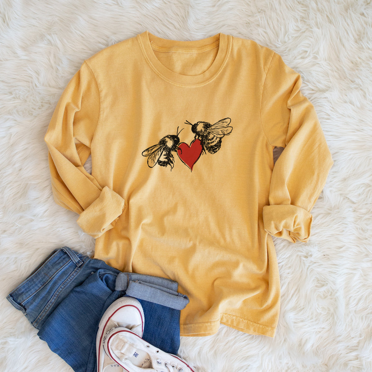 Golden wheat yellow Comfort Colors long sleeve shirt printed with a black ink illustration of two bees facing each other with a red heart between them, shown in a lifestyle photo.