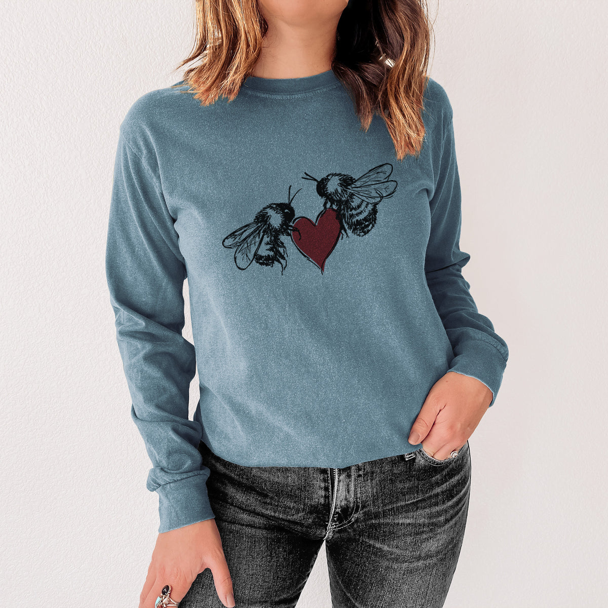 Steel blue Comfort Colors long sleeve shirt printed with a black ink illustration of two bees facing each other with a red heart between them, shown in a lifestyle photo.