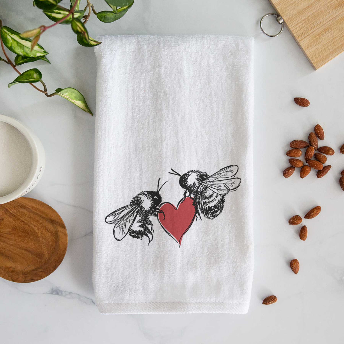 White hand towel printed with a black ink illustration of two bees facing each other with a red heart between them.