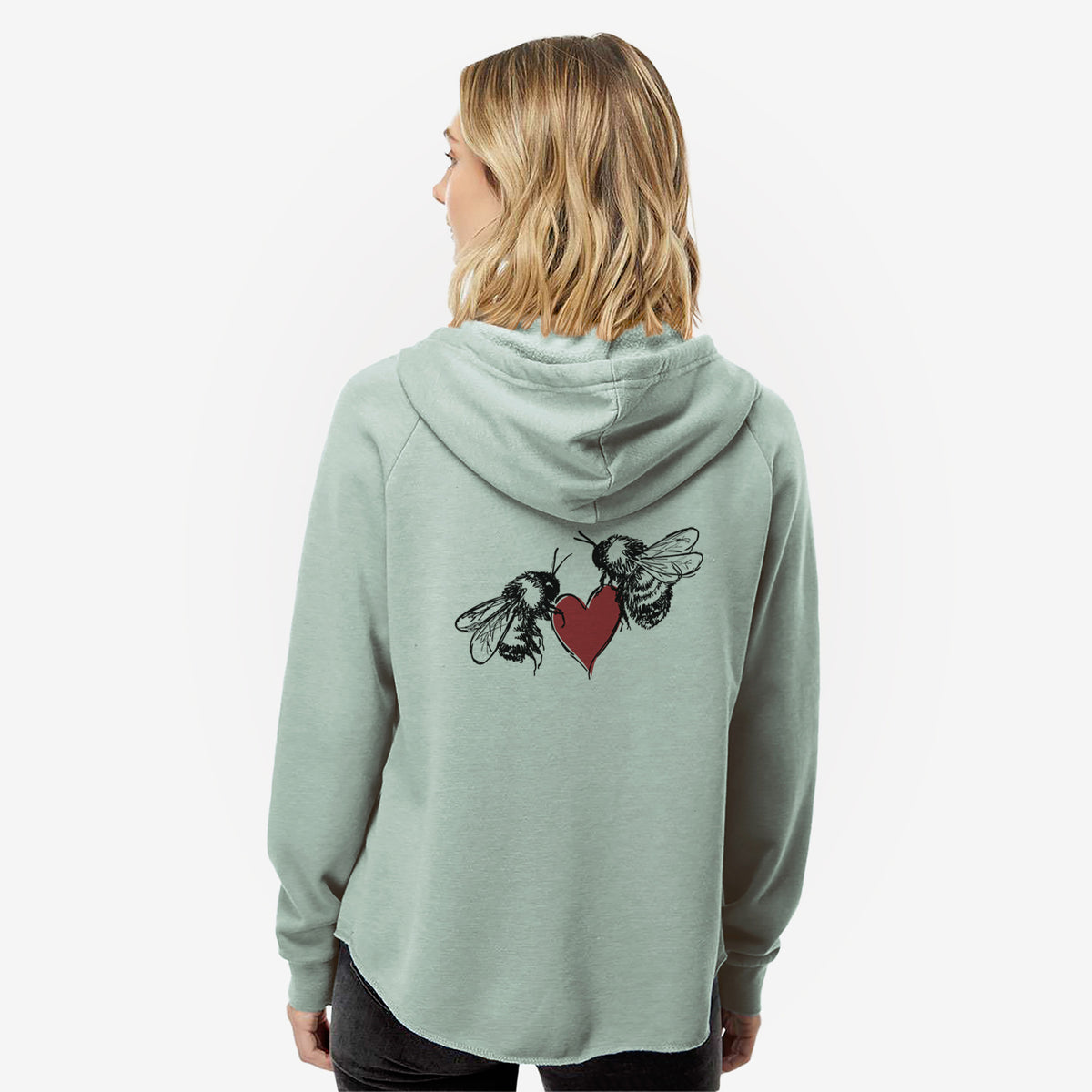 Woman wearing a sage green women's Cali Wave zip-up sweatshirt printed with a black ink illustration of two bees facing each other with a red heart between them, seen from behind.