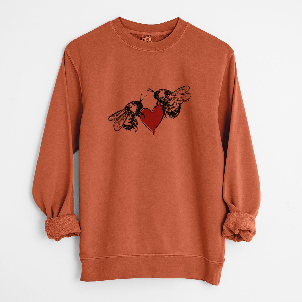 Amber orange pigment dyed crewneck sweatshirt laid flat with the sleeves rolled, printed with a black ink illustration of two bees facing each other with a red heart between them.
