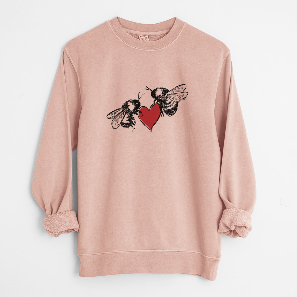 Dusty pink pigment dyed crewneck sweatshirt laid flat with the sleeves rolled, printed with a black ink illustration of two bees facing each other with a red heart between them.