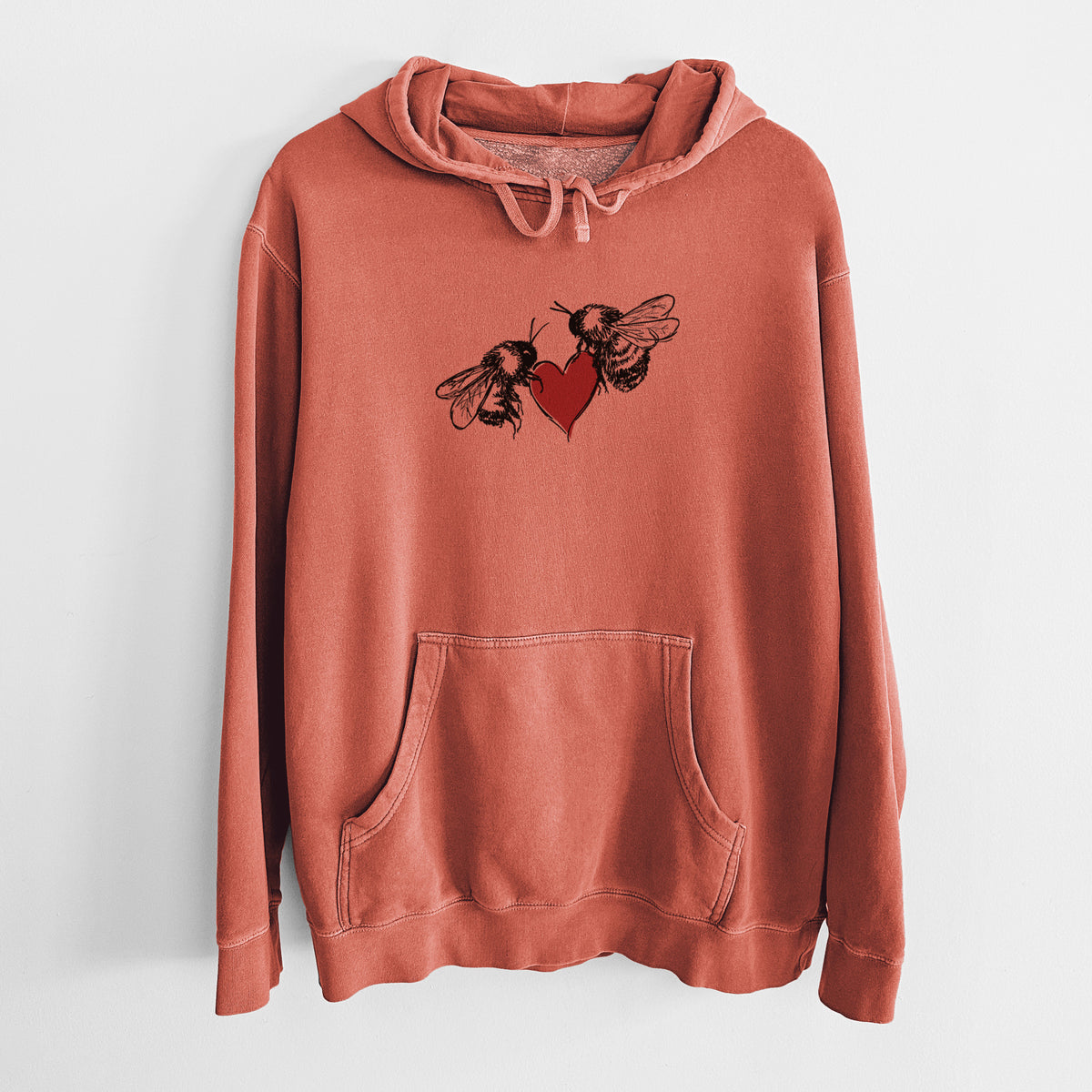 Amber orange pigment dyed hoodie laid flat, printed with a black ink illustration of two bees facing each other with a red heart between them.