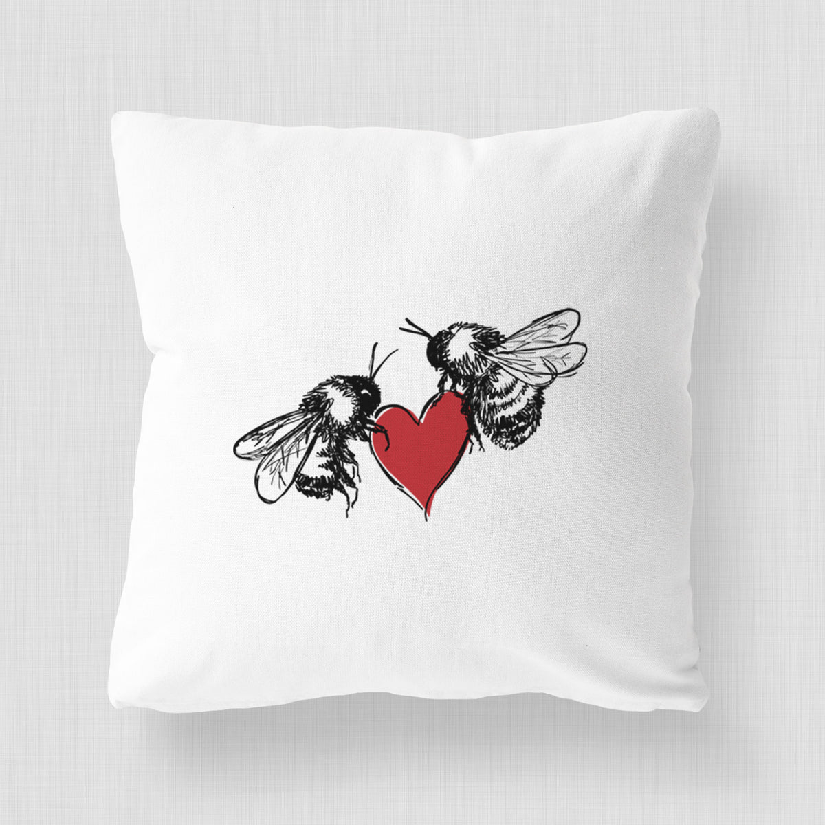 White pillow cover printed with a black ink illustration of two bees facing each other with a red heart between them.