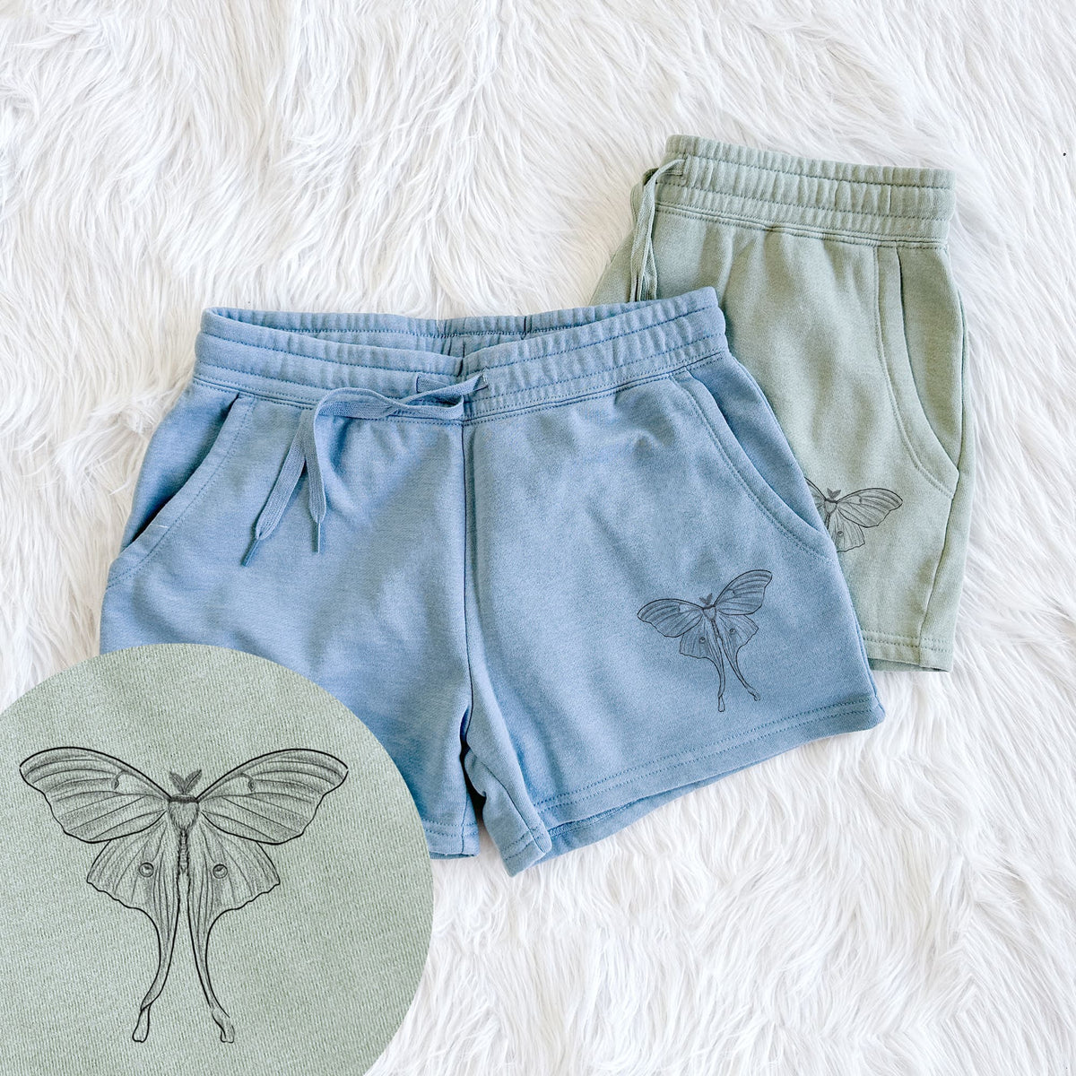 Two pairs of Cali Wave shorts in different colors printed with a black ink line drawing of a luna moth with long trailing tails on its wings, with a close-up of the print.