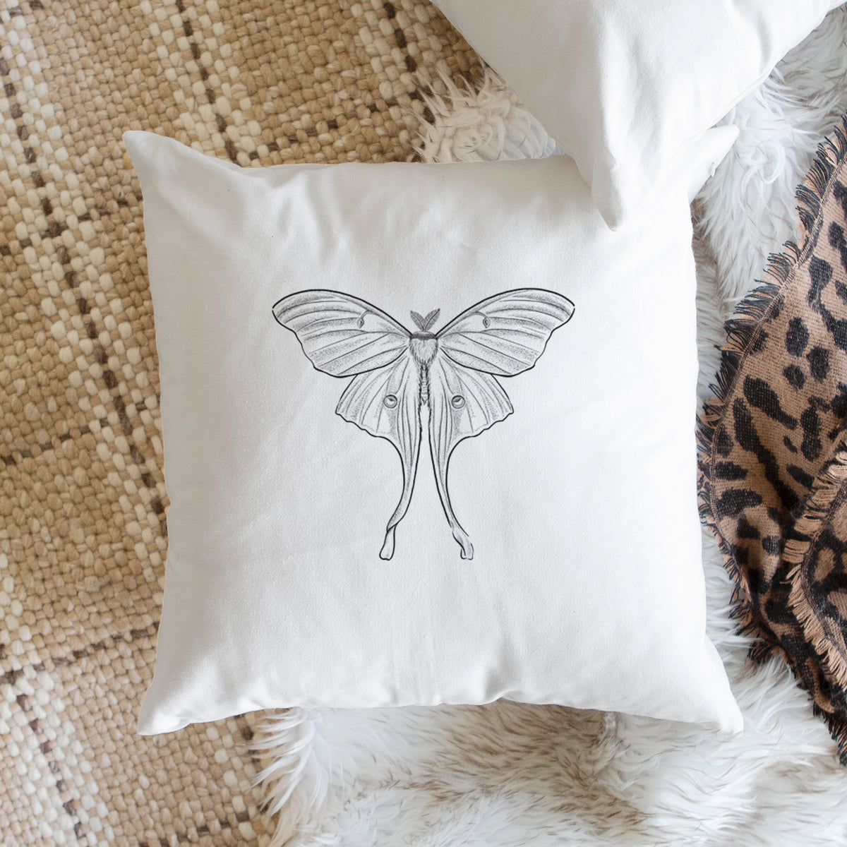 White pillow cover printed with a black ink line drawing of a luna moth with long trailing tails on its wings, on a woven chair.
