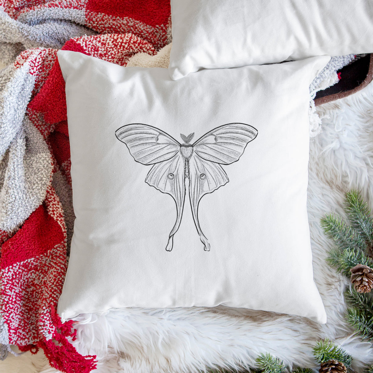 White pillow cover printed with a black ink line drawing of a luna moth with long trailing tails on its wings, on a woven chair.