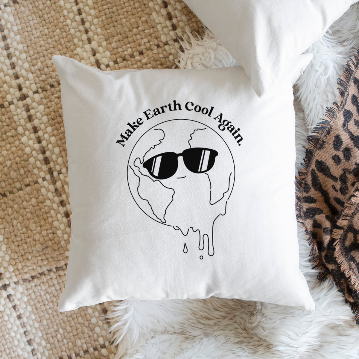 White pillow cover printed with a melting Earth wearing black sunglasses, with the words Make Earth Cool Again, on a woven chair.