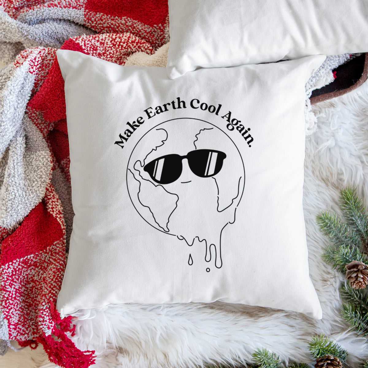 White pillow cover printed with a melting Earth wearing black sunglasses, with the words Make Earth Cool Again, on a woven chair.