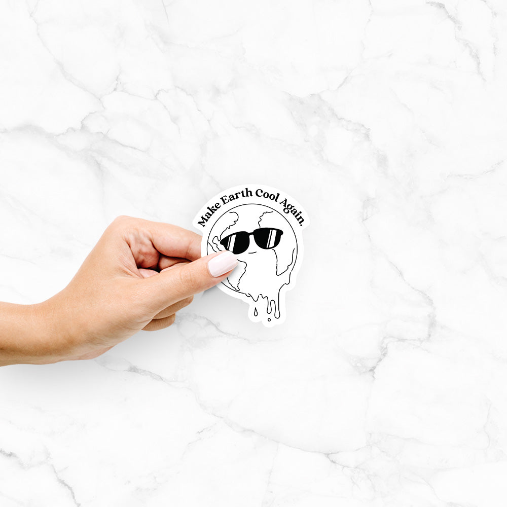Hand holding a 4 inch vinyl decal of a melting Earth wearing black sunglasses, with the words Make Earth Cool Again.