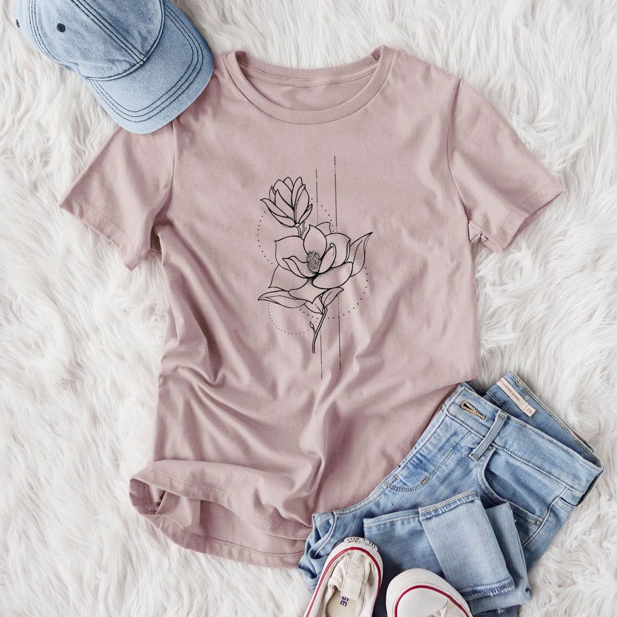 Women's relaxed fit cotton t-shirt printed with a black ink line drawing of a magnolia blossom on a stem, styled flat on a white faux fur rug with jeans.