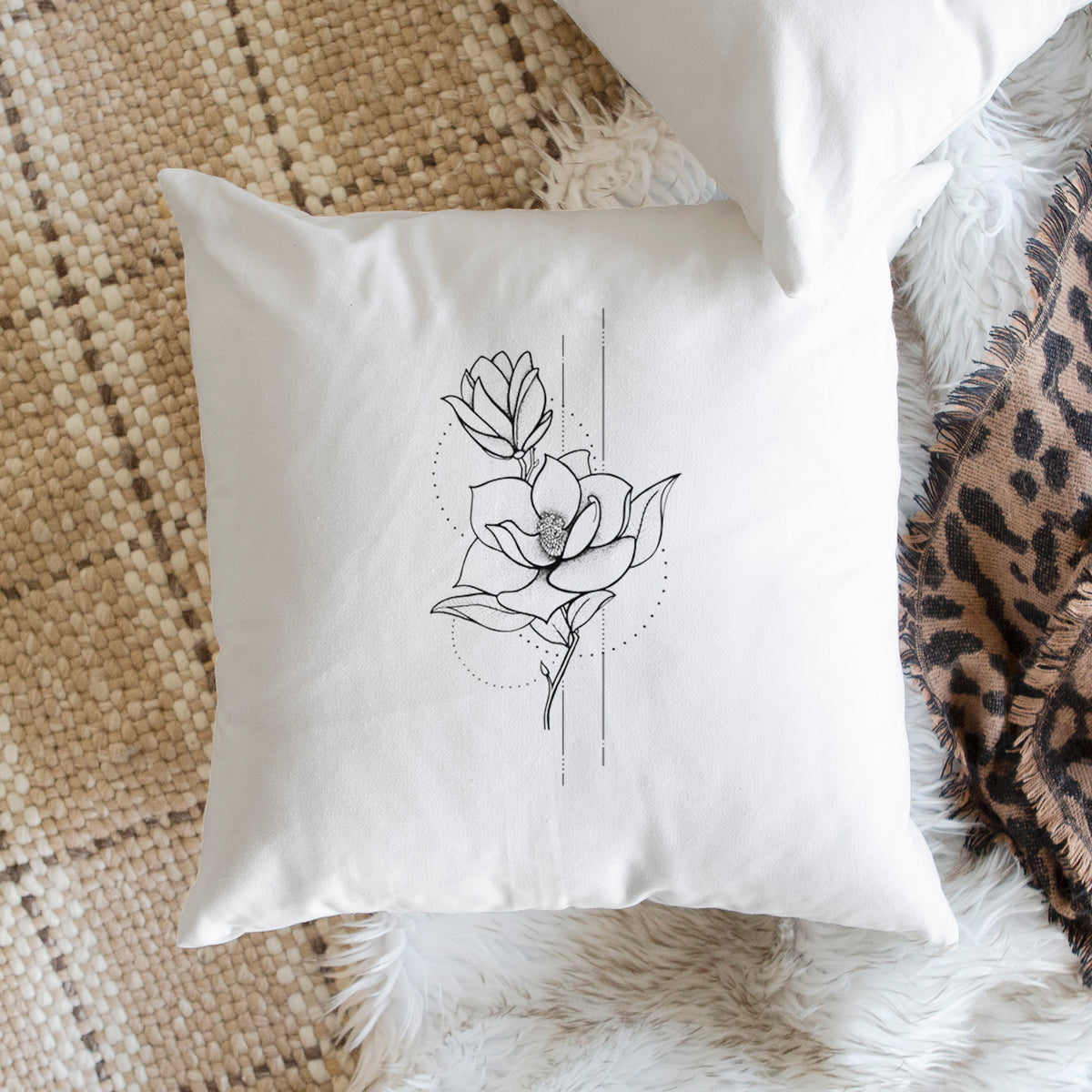White pillow cover printed with a black ink line drawing of a magnolia blossom on a stem, on a woven chair.