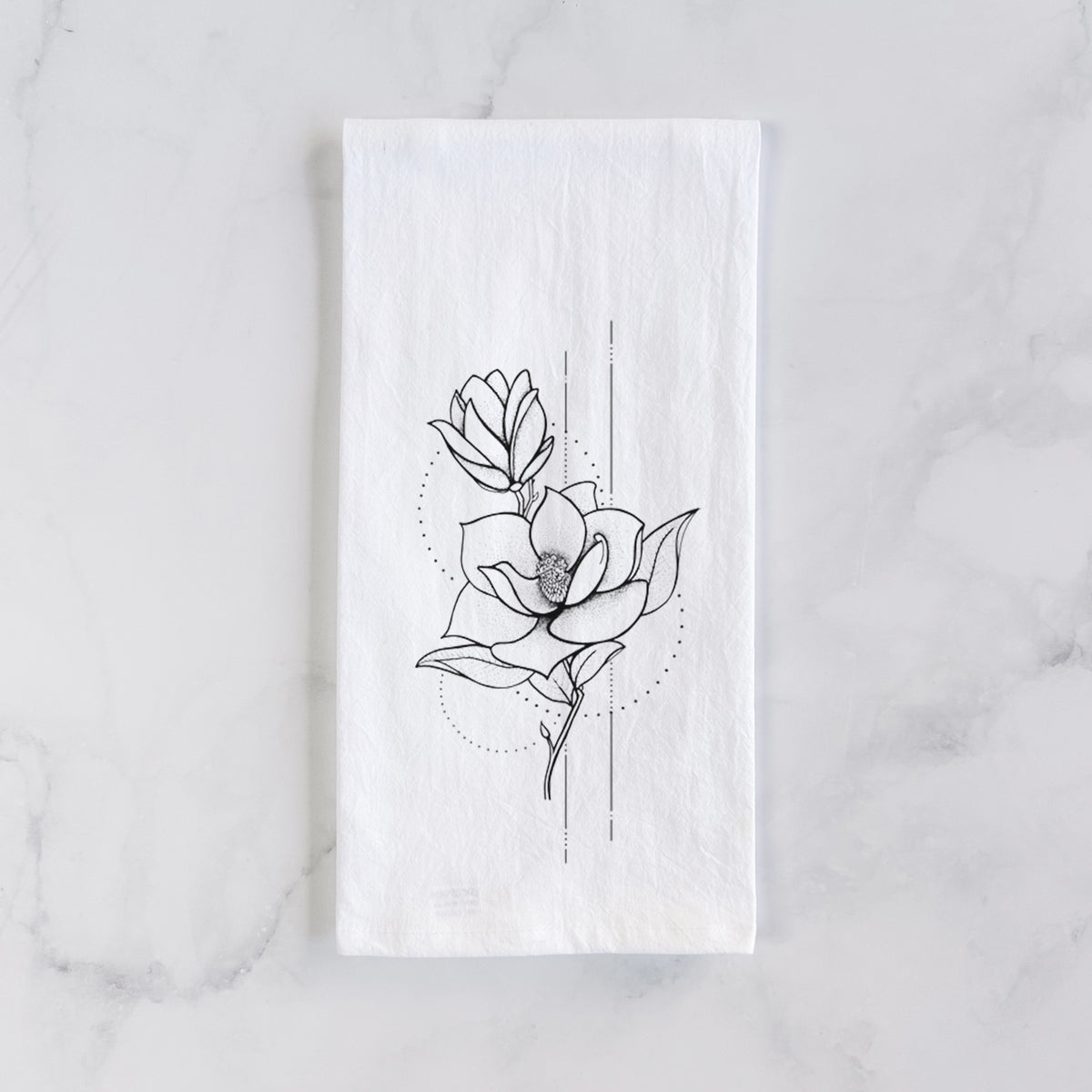 White cotton tea towel laid flat on marble, printed with a black ink line drawing of a magnolia blossom on a stem.