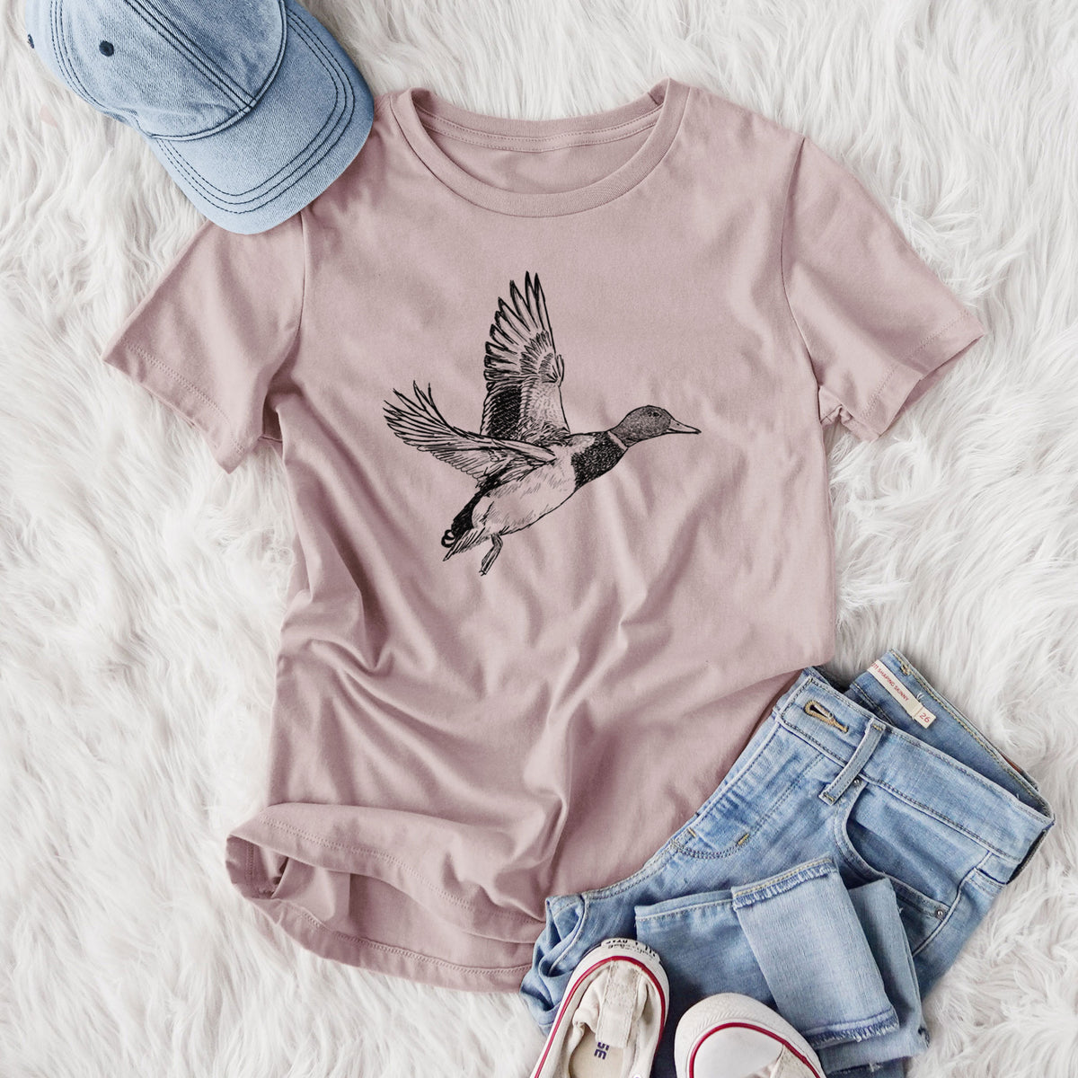 Women's relaxed fit cotton t-shirt printed with a detailed black ink illustration of a male mallard duck taking flight, styled flat on a white faux fur rug with jeans.
