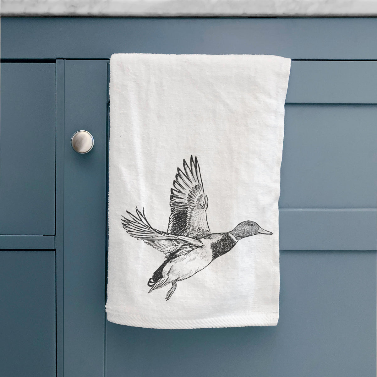 White hand towel printed with a detailed black ink illustration of a male mallard duck taking flight, hanging on a cabinet door.