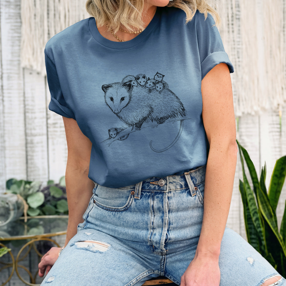 Woman wearing a steel blue lightweight cotton t-shirt printed with a black ink illustration of a mother opossum on a branch carrying her babies on her back.