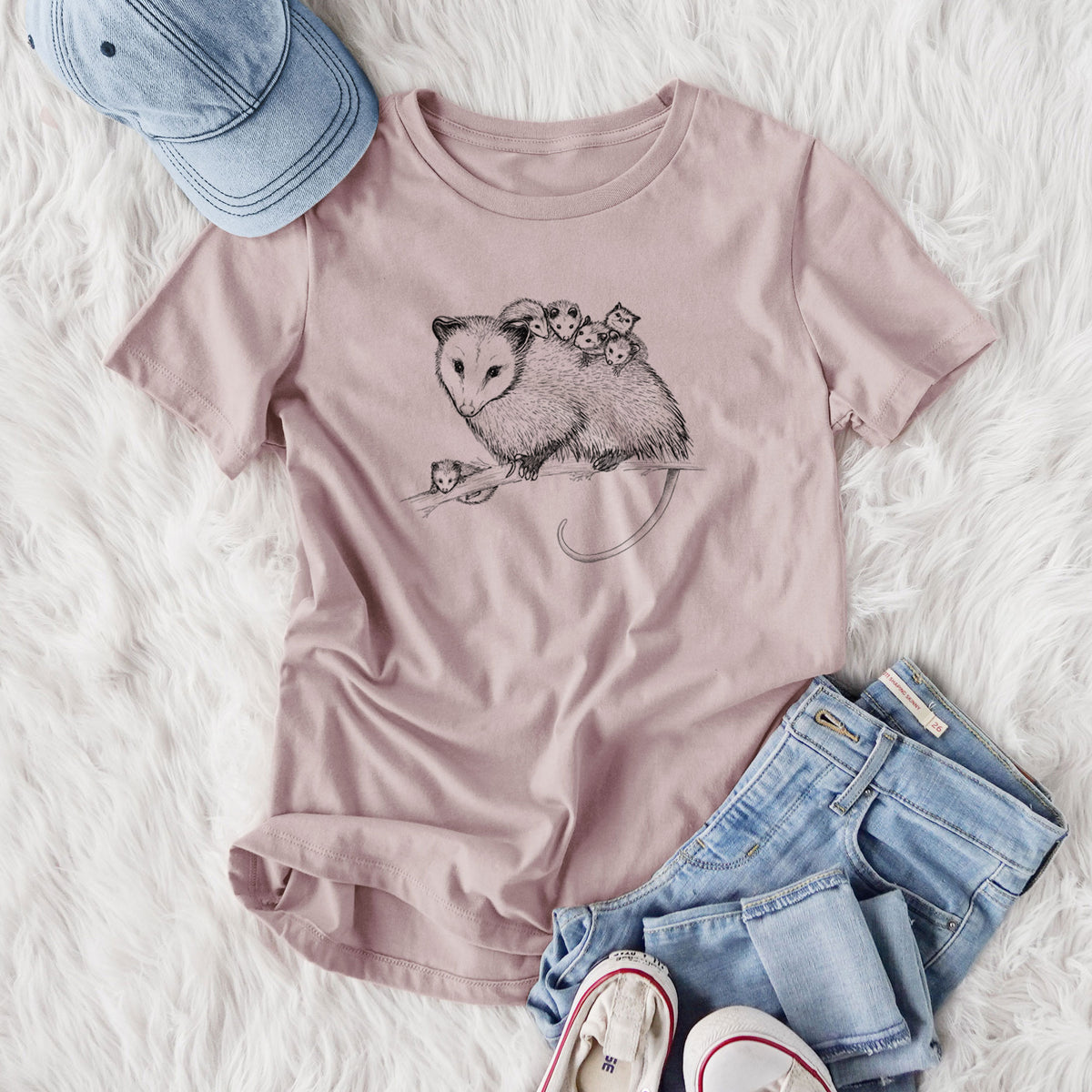 Women's relaxed fit cotton t-shirt printed with a black ink illustration of a mother opossum on a branch carrying her babies on her back, styled flat on a white faux fur rug with jeans.