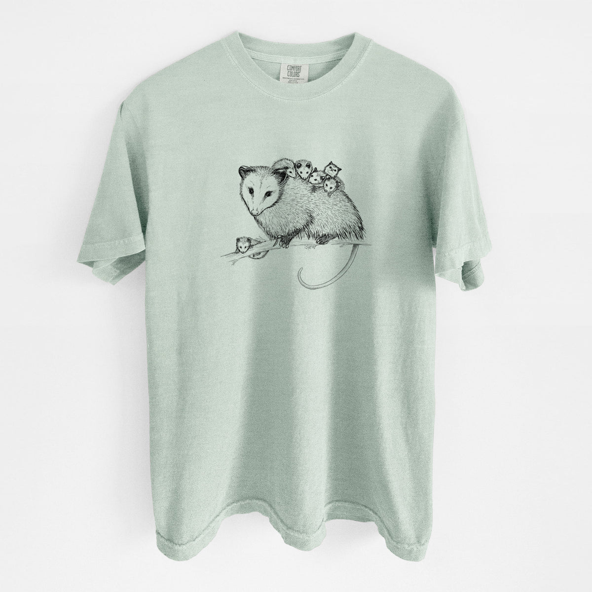 Bay green Comfort Colors t-shirt laid flat, printed with a black ink illustration of a mother opossum on a branch carrying her babies on her back.