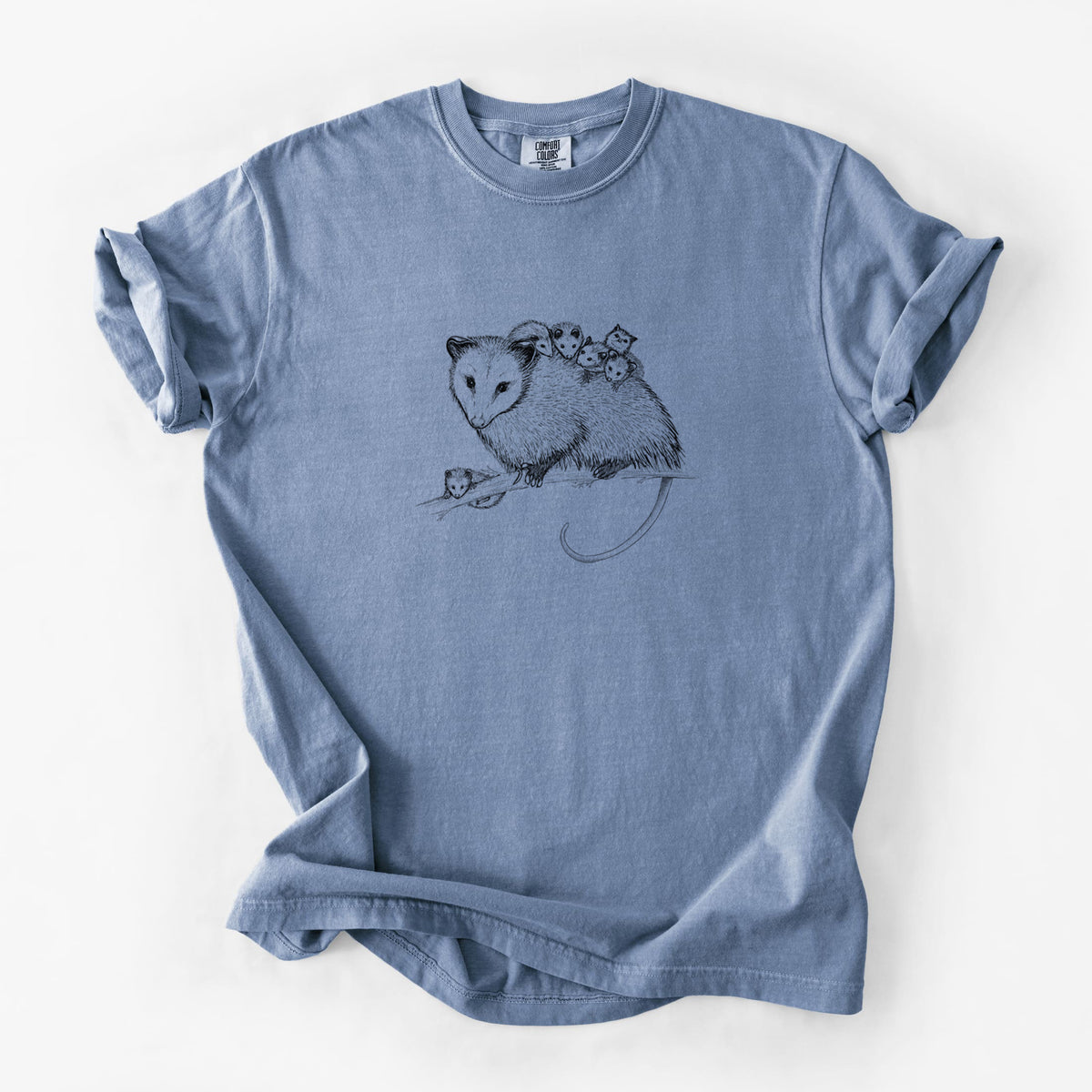 Blue jean Comfort Colors t-shirt laid flat, printed with a black ink illustration of a mother opossum on a branch carrying her babies on her back.