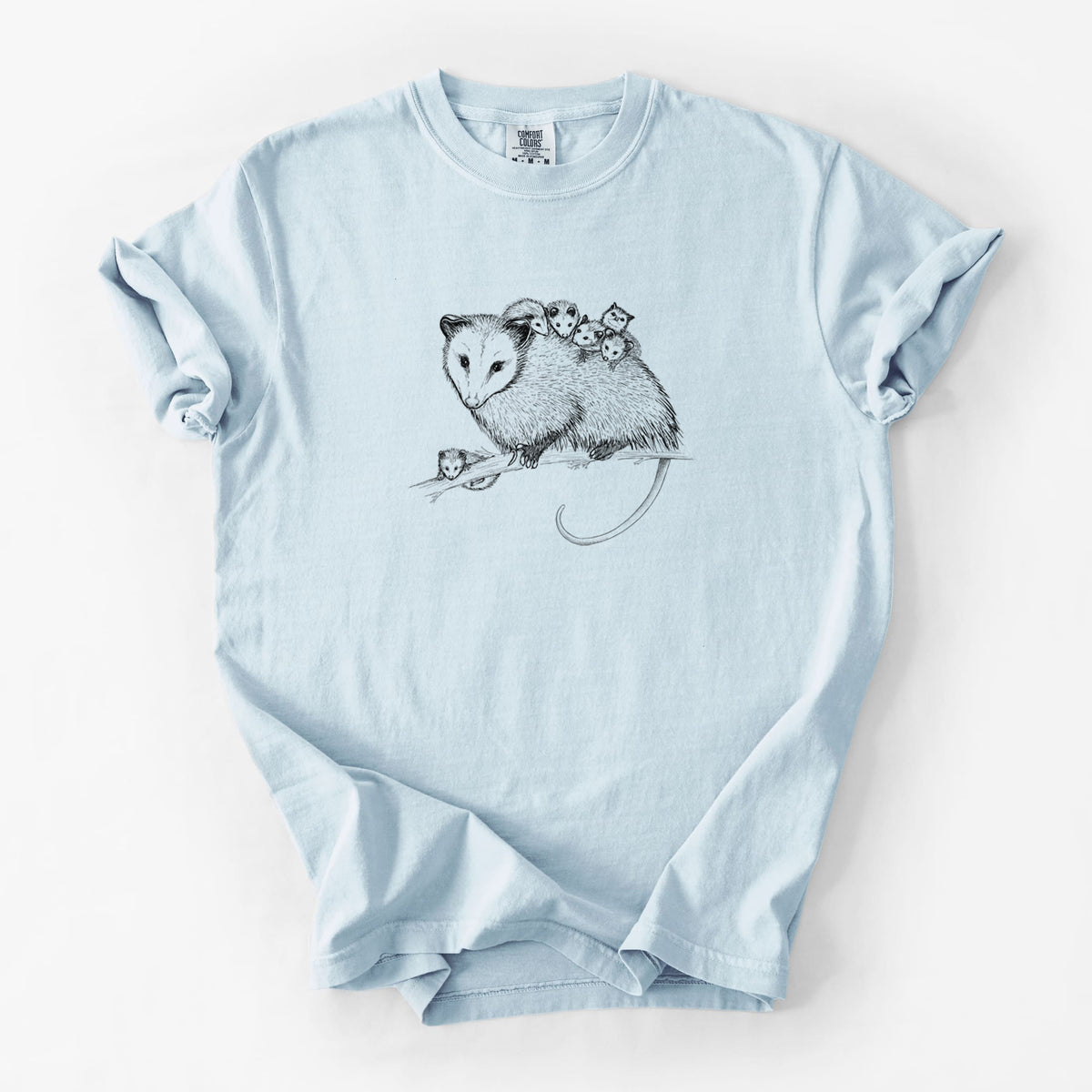 Chambray blue Comfort Colors t-shirt laid flat, printed with a black ink illustration of a mother opossum on a branch carrying her babies on her back.