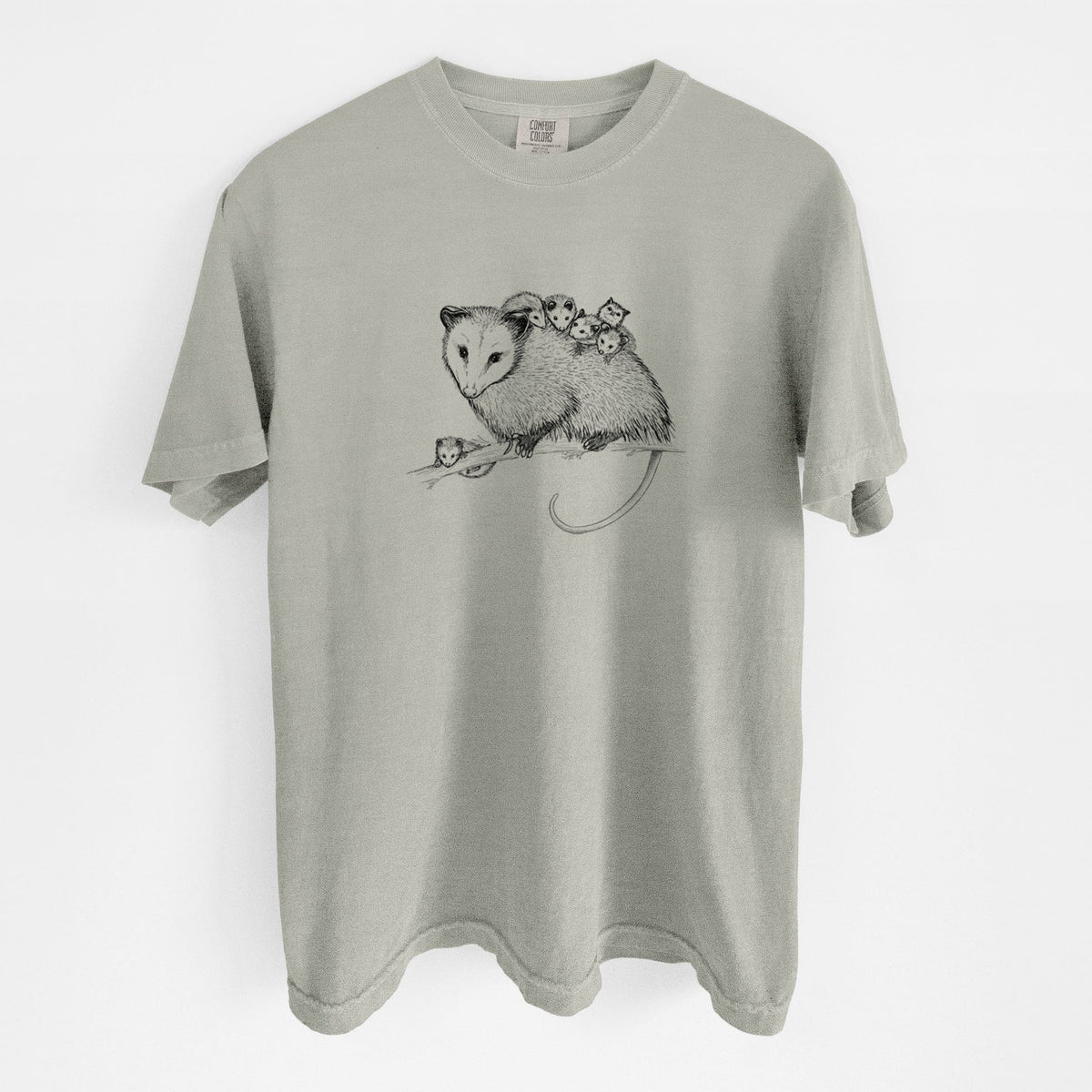 Sandstone beige Comfort Colors t-shirt laid flat, printed with a black ink illustration of a mother opossum on a branch carrying her babies on her back.