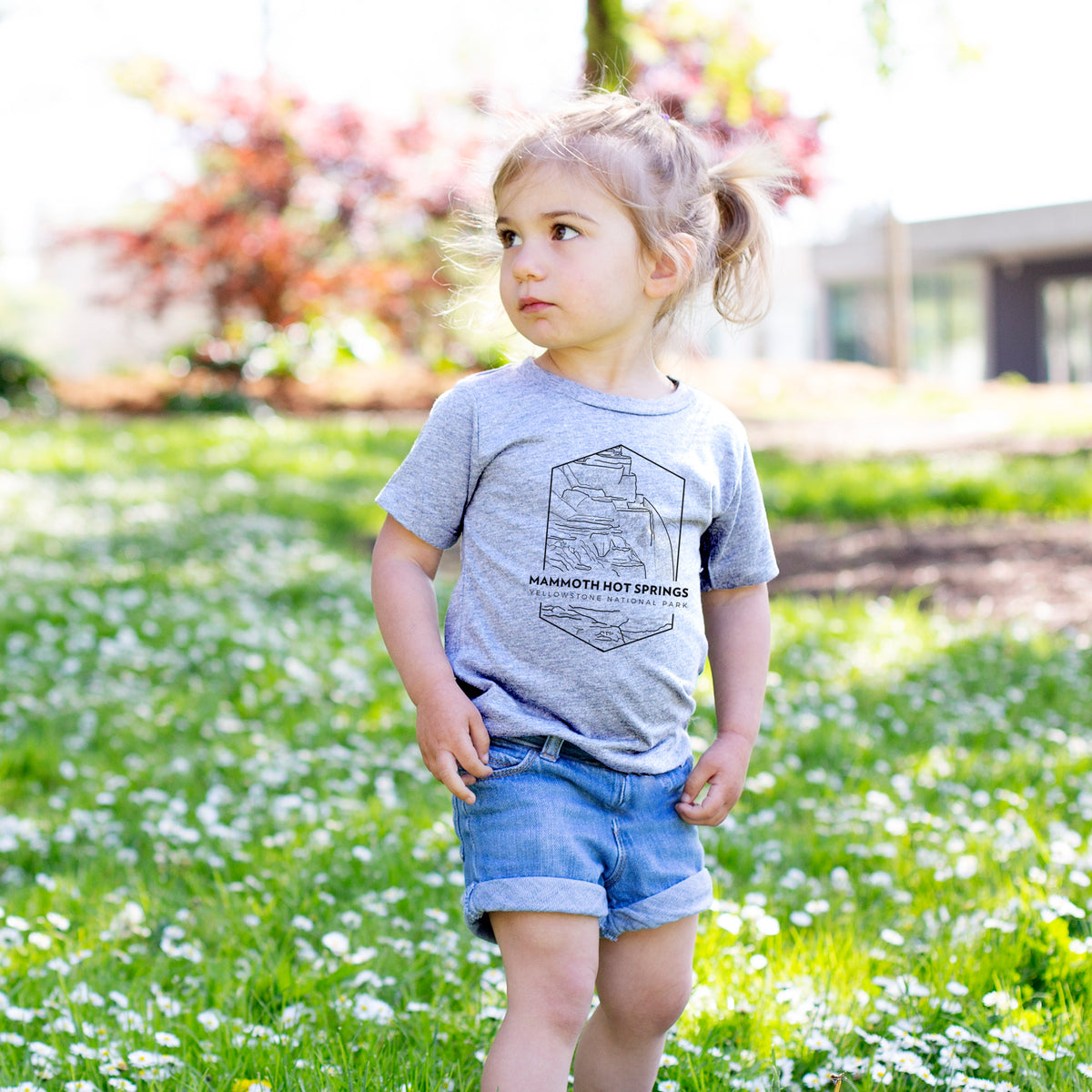 Toddler girl walking outdoors wearing a t-shirt printed with a black line art badge of the terraces at Mammoth Hot Springs, with the words Mammoth Hot Springs, Yellowstone National Park.