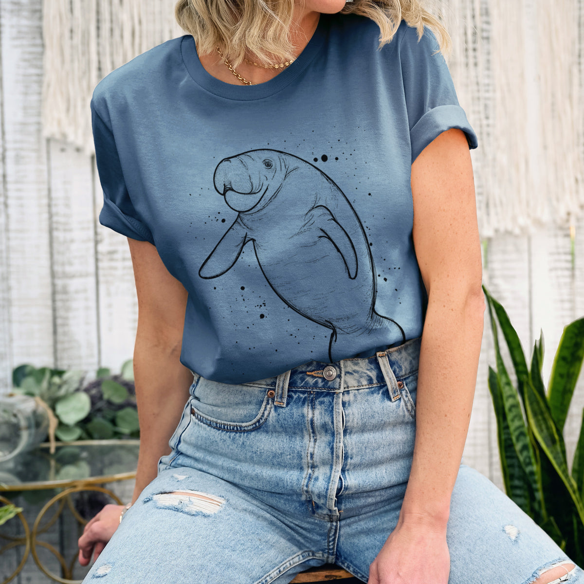 Woman wearing a steel blue lightweight cotton t-shirt printed with a black ink line drawing of a manatee swimming, with ink splatters.