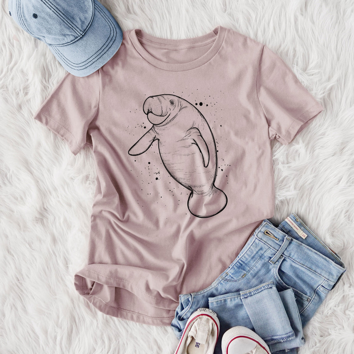 Women's relaxed fit cotton t-shirt printed with a black ink line drawing of a manatee swimming, with ink splatters, styled flat on a white faux fur rug with jeans.