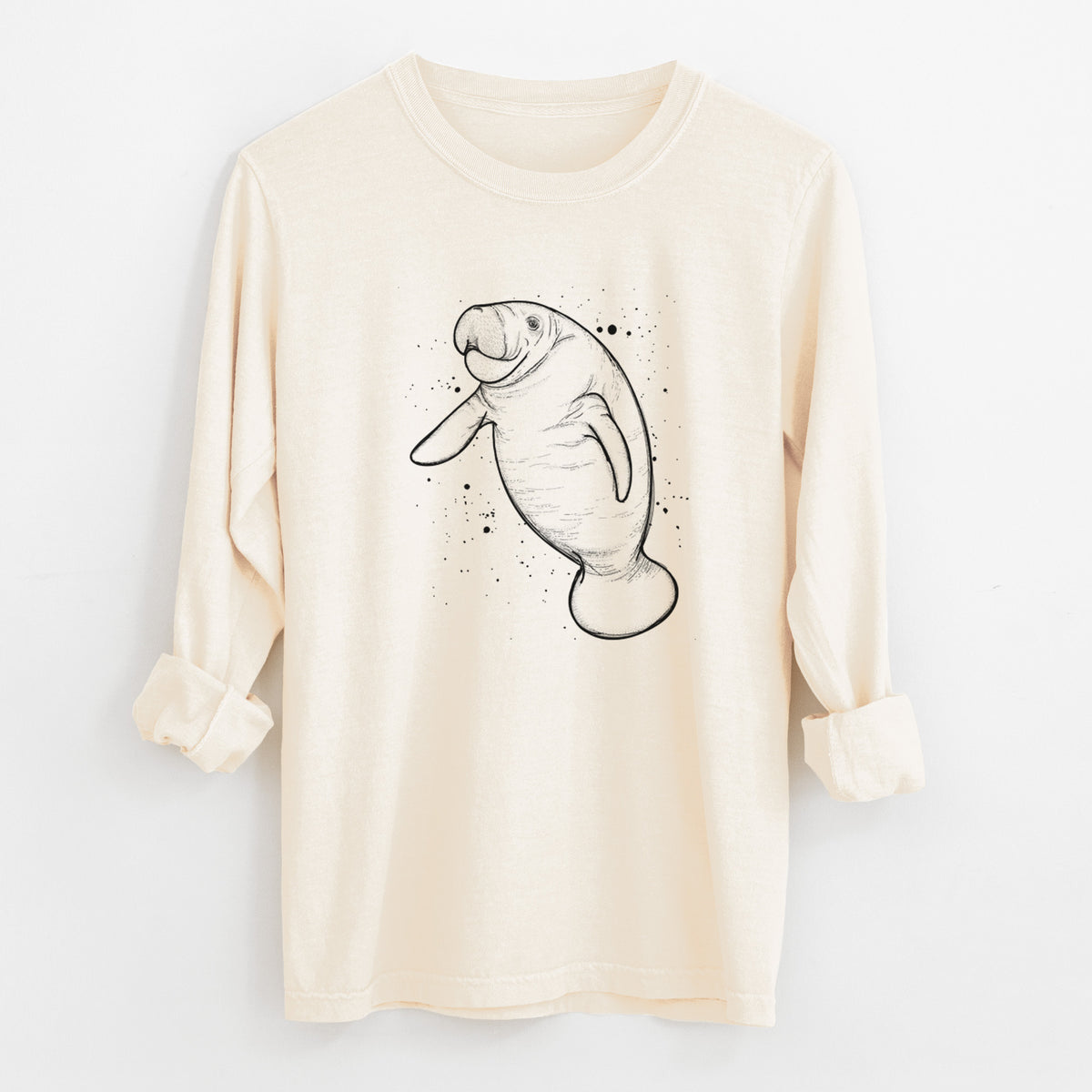 Ivory Comfort Colors long sleeve shirt laid flat with the cuffs rolled, printed with a black ink line drawing of a manatee swimming, with ink splatters.