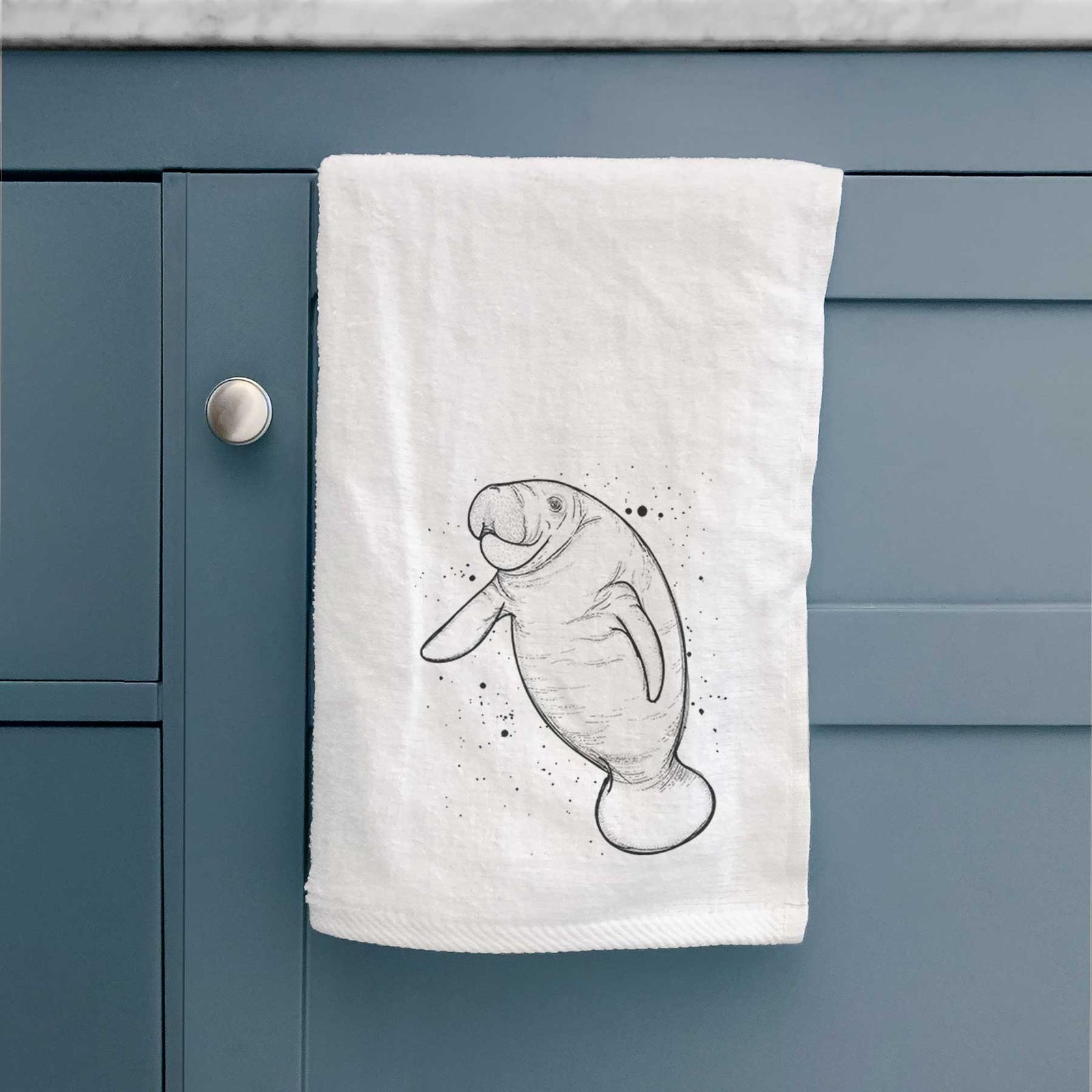 White hand towel printed with a black ink line drawing of a manatee swimming, with ink splatters.