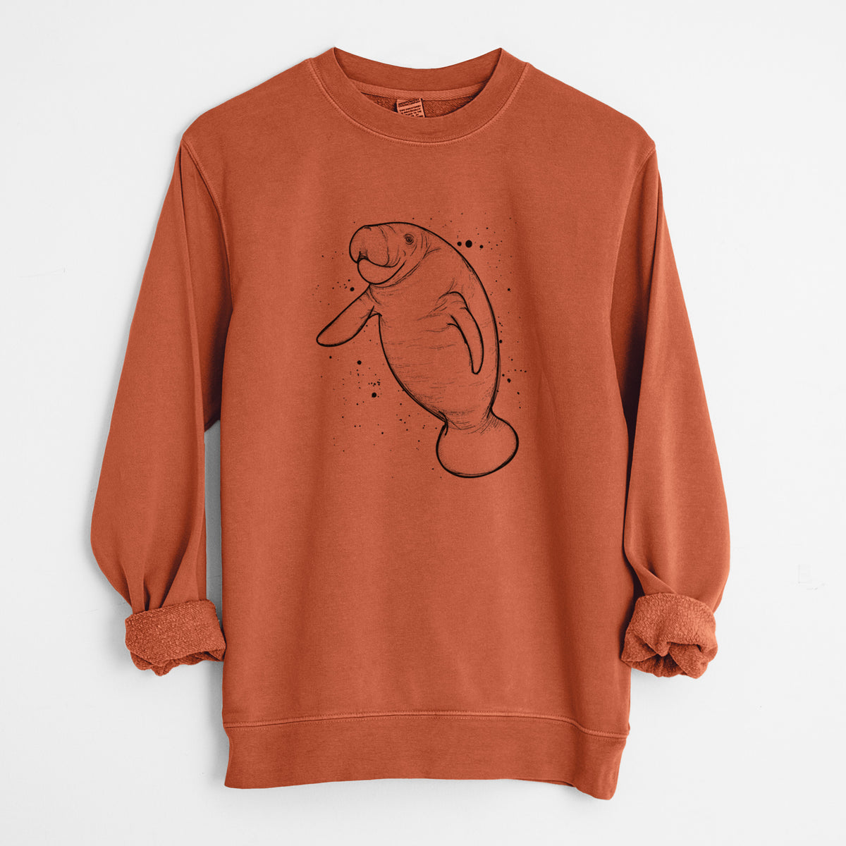 Amber orange pigment dyed crewneck sweatshirt laid flat with the sleeves rolled, printed with a black ink line drawing of a manatee swimming, with ink splatters.