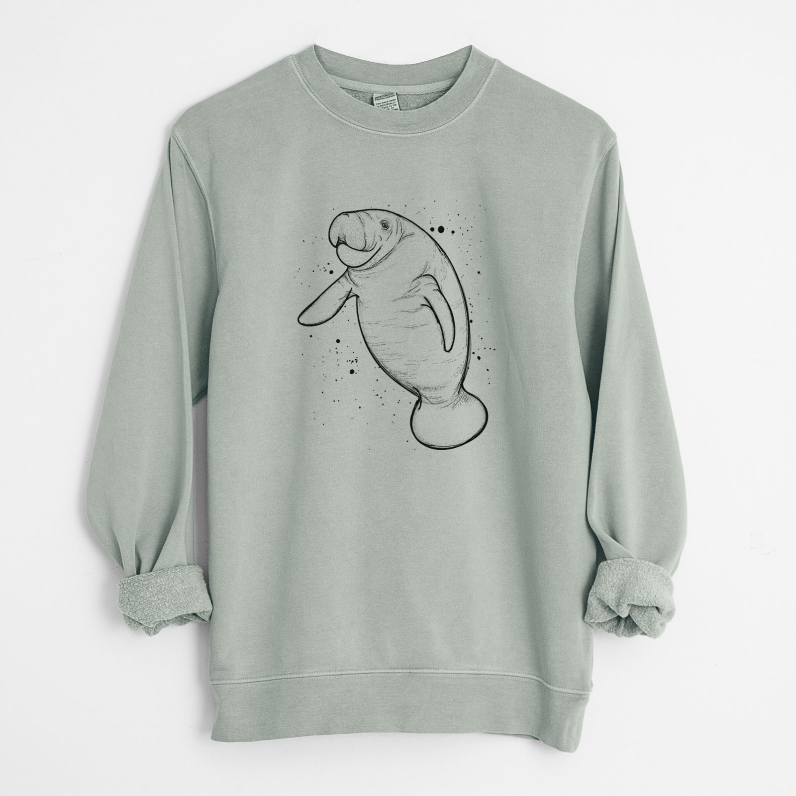 Sage green pigment dyed crewneck sweatshirt laid flat with the sleeves rolled, printed with a black ink line drawing of a manatee swimming, with ink splatters.